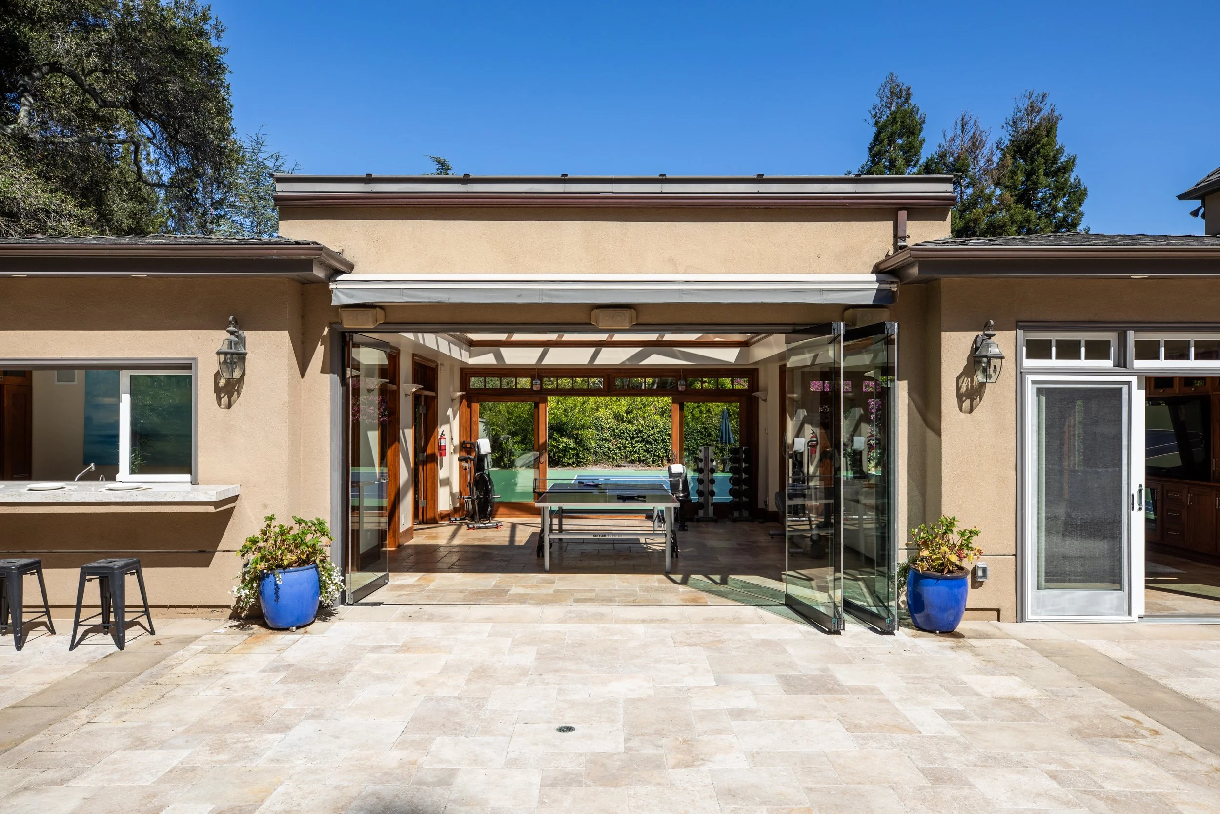 Open sliding glass doors leading from a patio to a backyard gym with workout equipment.