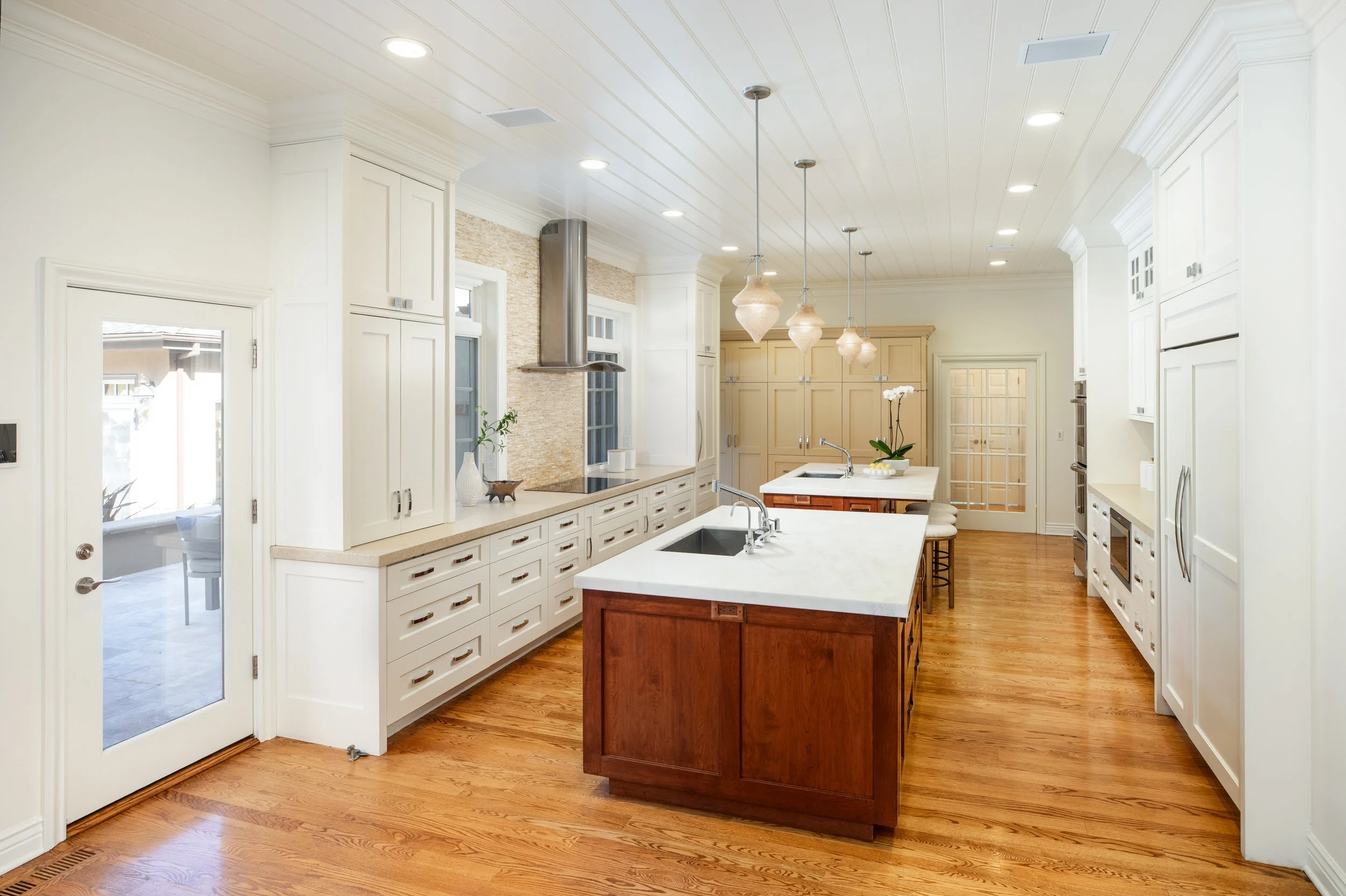 Bright kitchen with white cabinets, a central island with a darker wood base, pendant lights, and hardwood floors.