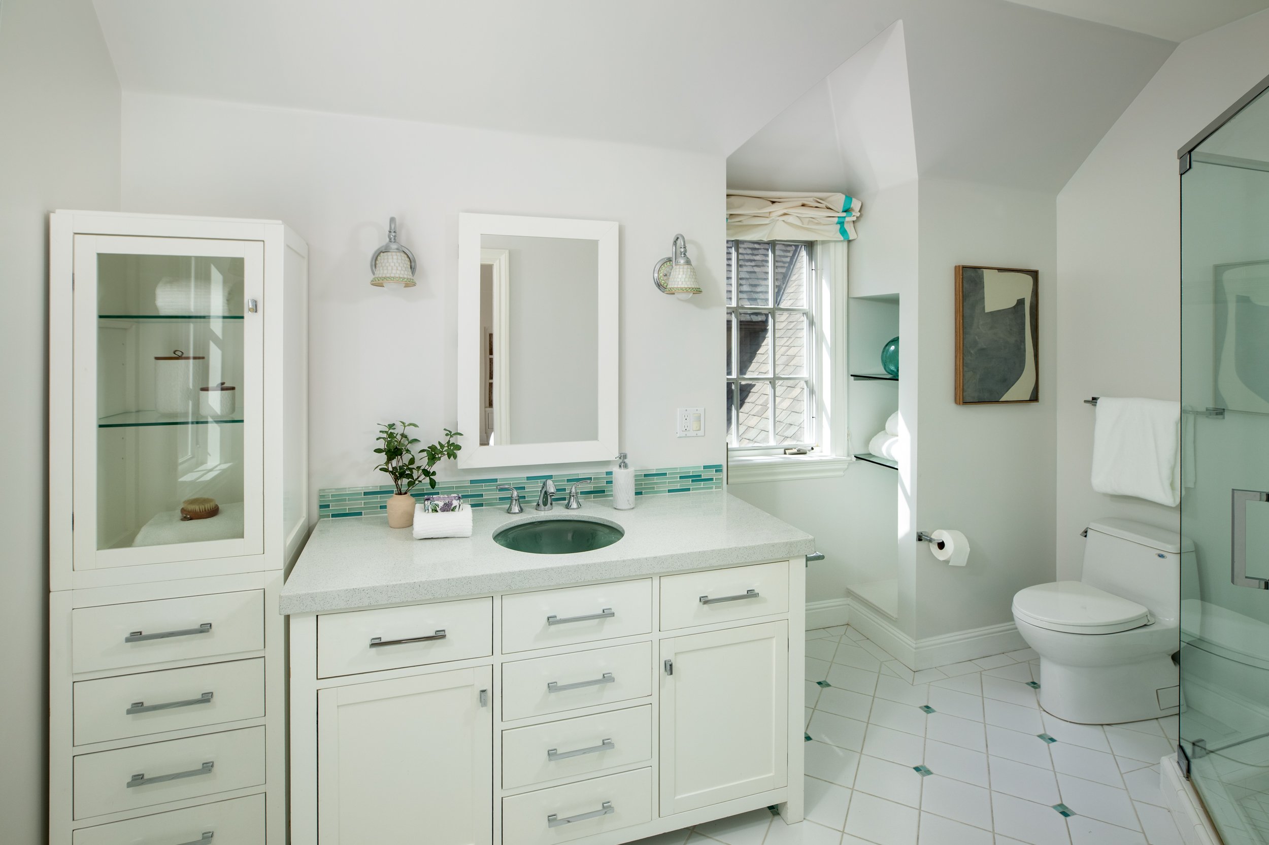 Bright white bathroom with a vanity, mirror, and a small window in the background.