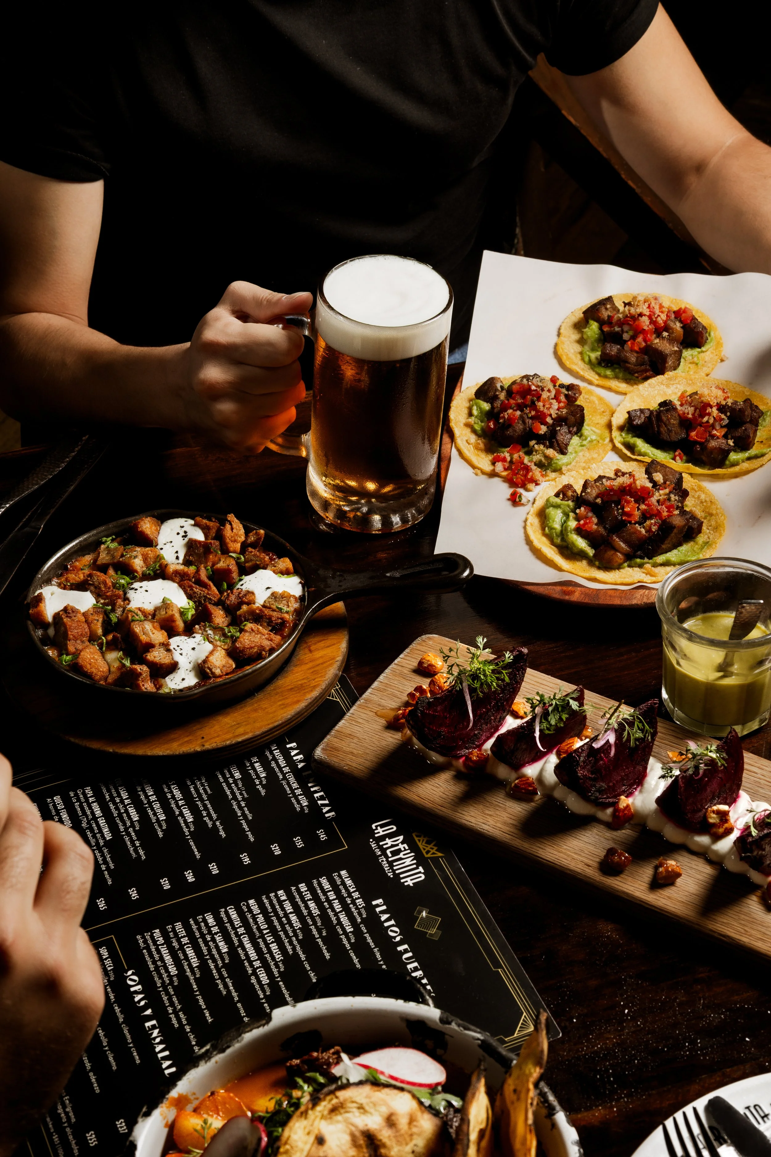 Persona con una jarra de cerveza frente a una mesa con alimentos.