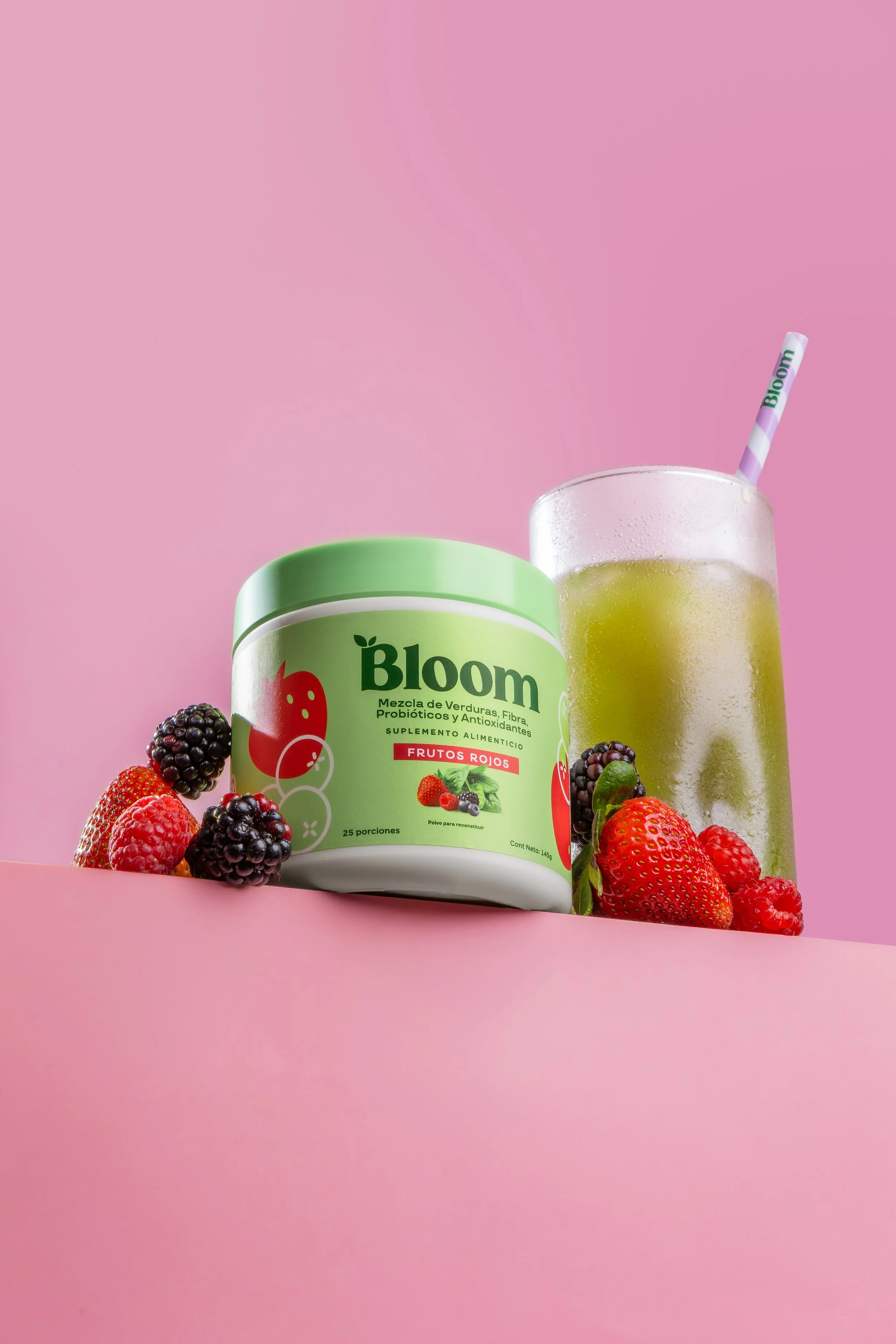 Producto Bloom con frutos rojos y bebida verde sobre fondo rosa.