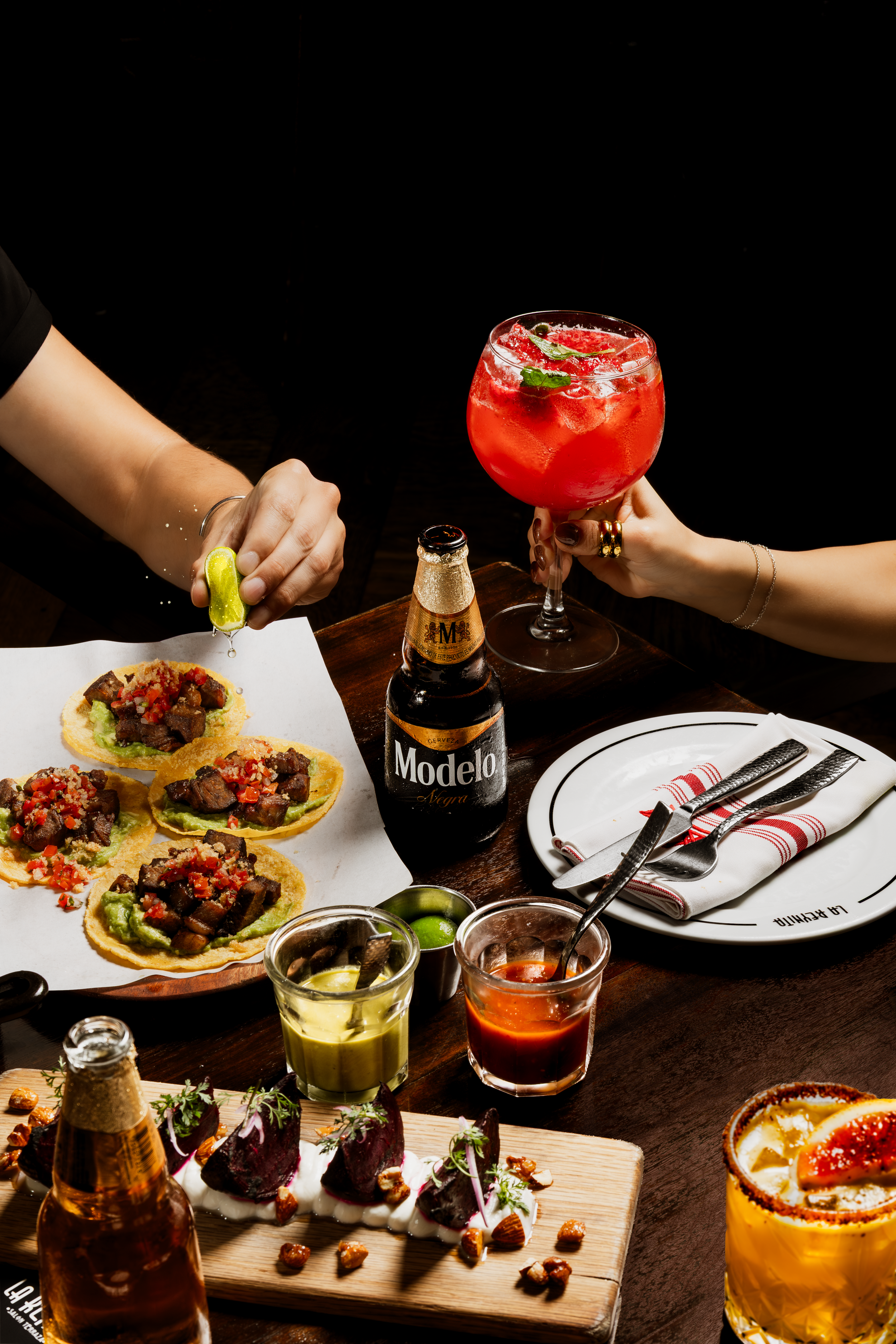 Mesa de restaurante con tacos, cócteles y cervezas.