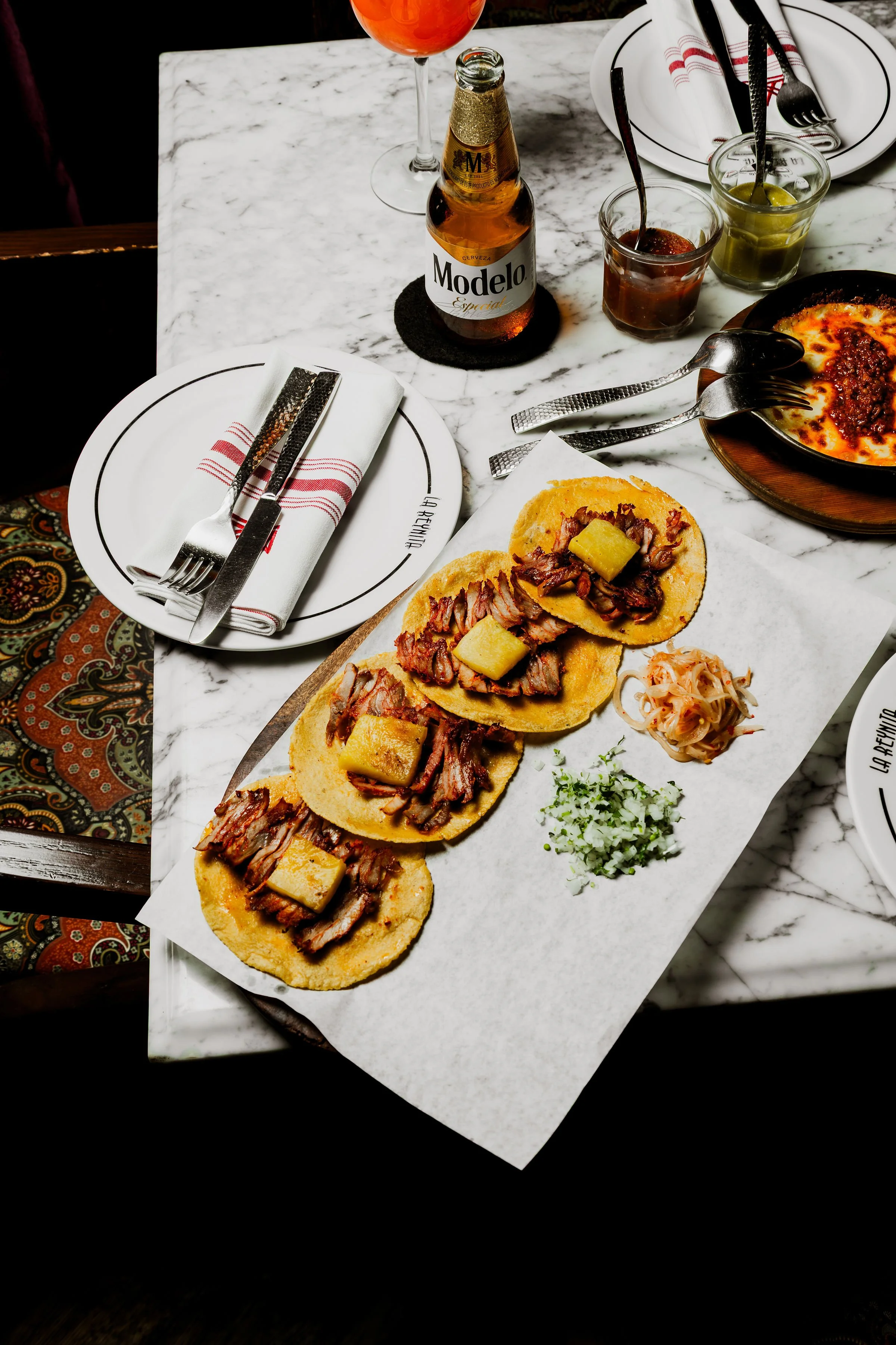 Tacos con piña, cebolla y cilantro acompañados de salsas y bebidas.