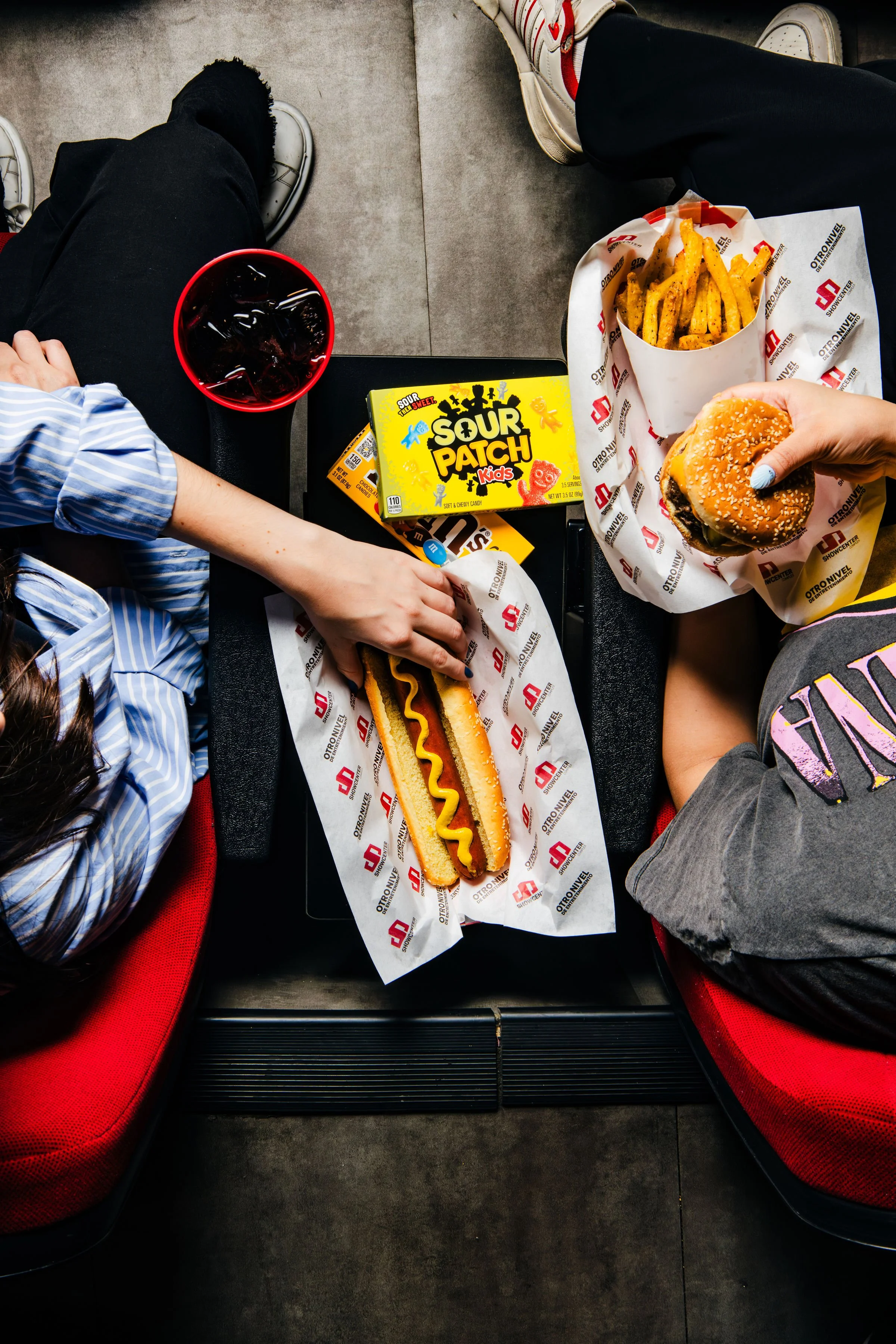 Personas compartiendo hamburguesa, hot dog y papas en el cine.
