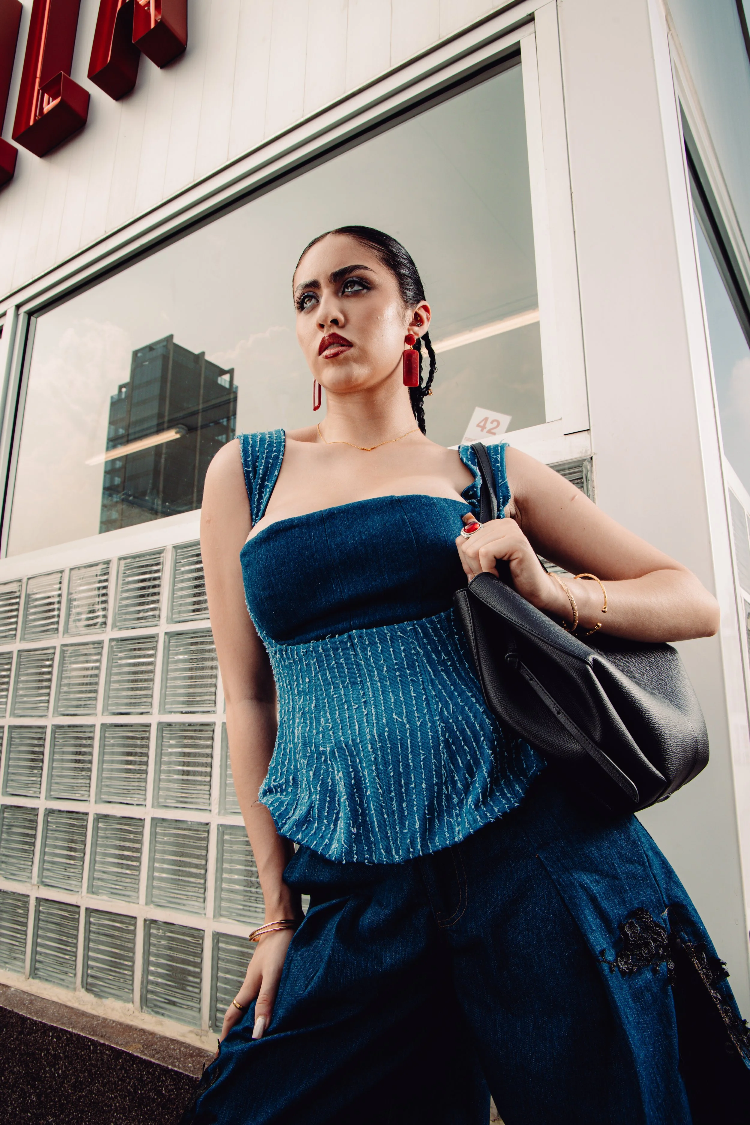 Modelo con vestido azul, accesorios rojos y bolso negro en exteriores.