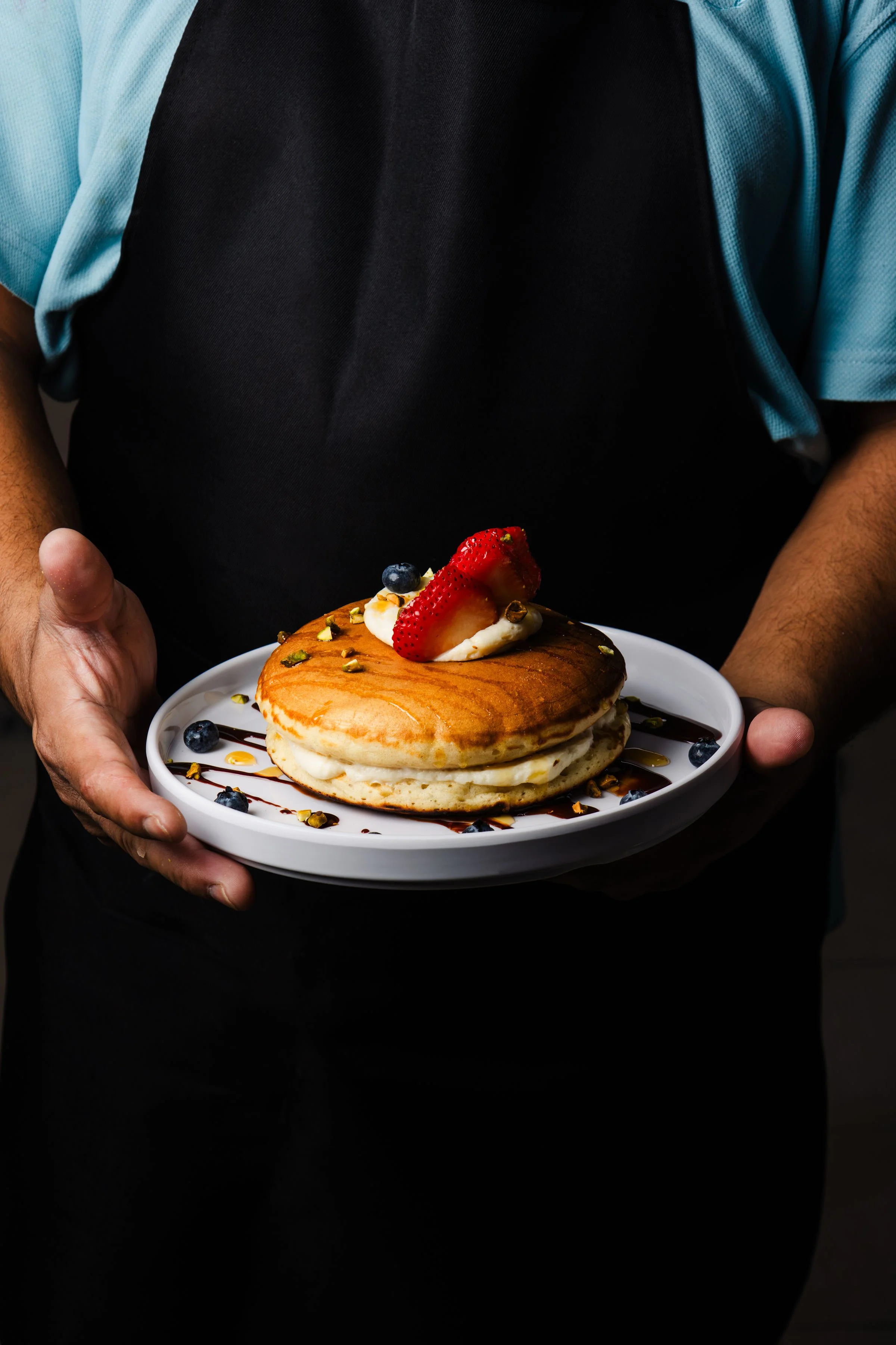 Hot cakes con crema, frutos rojos y pistache servidos en un plato.