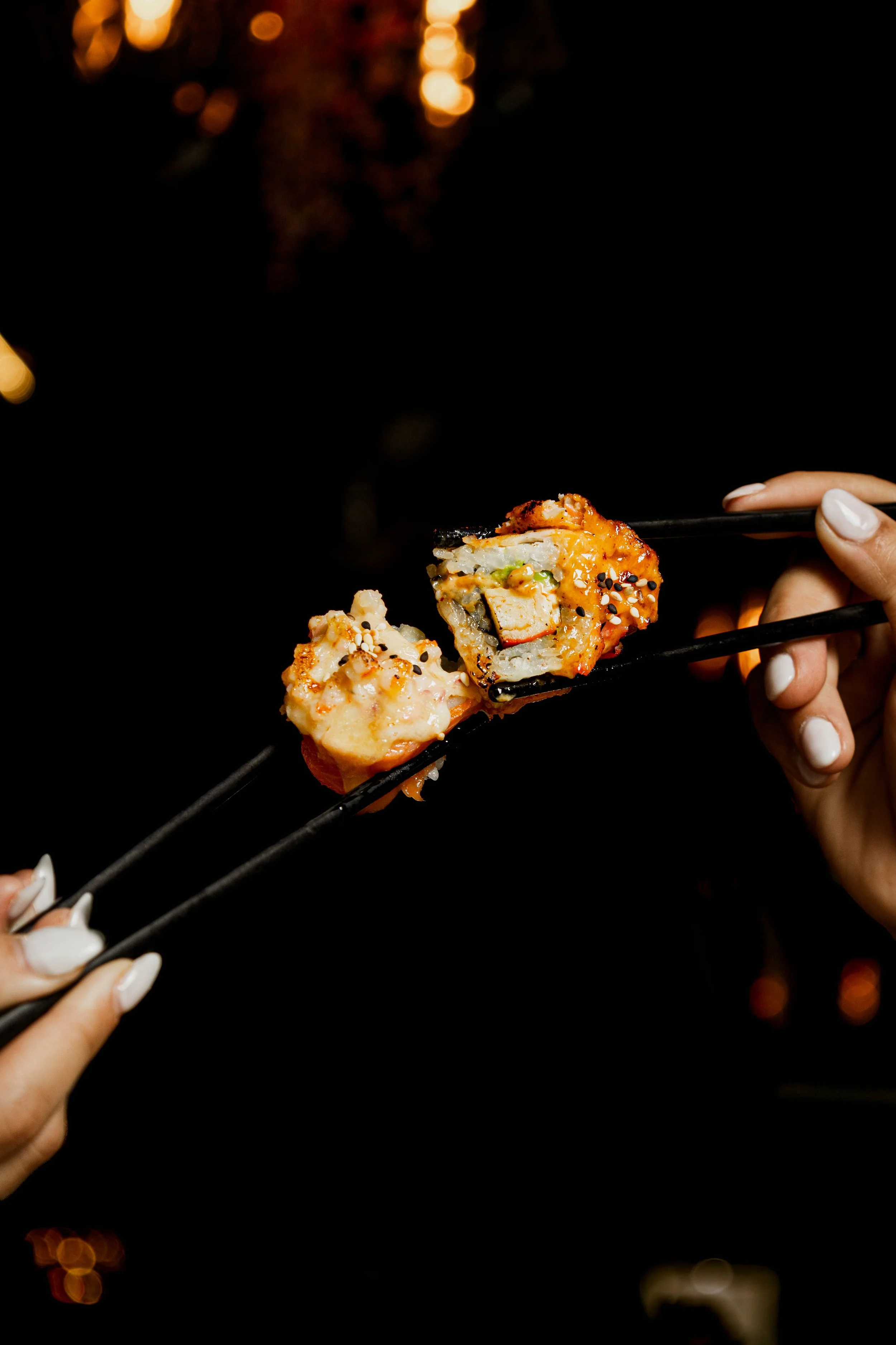 Manos sosteniendo piezas de sushi con palillos.