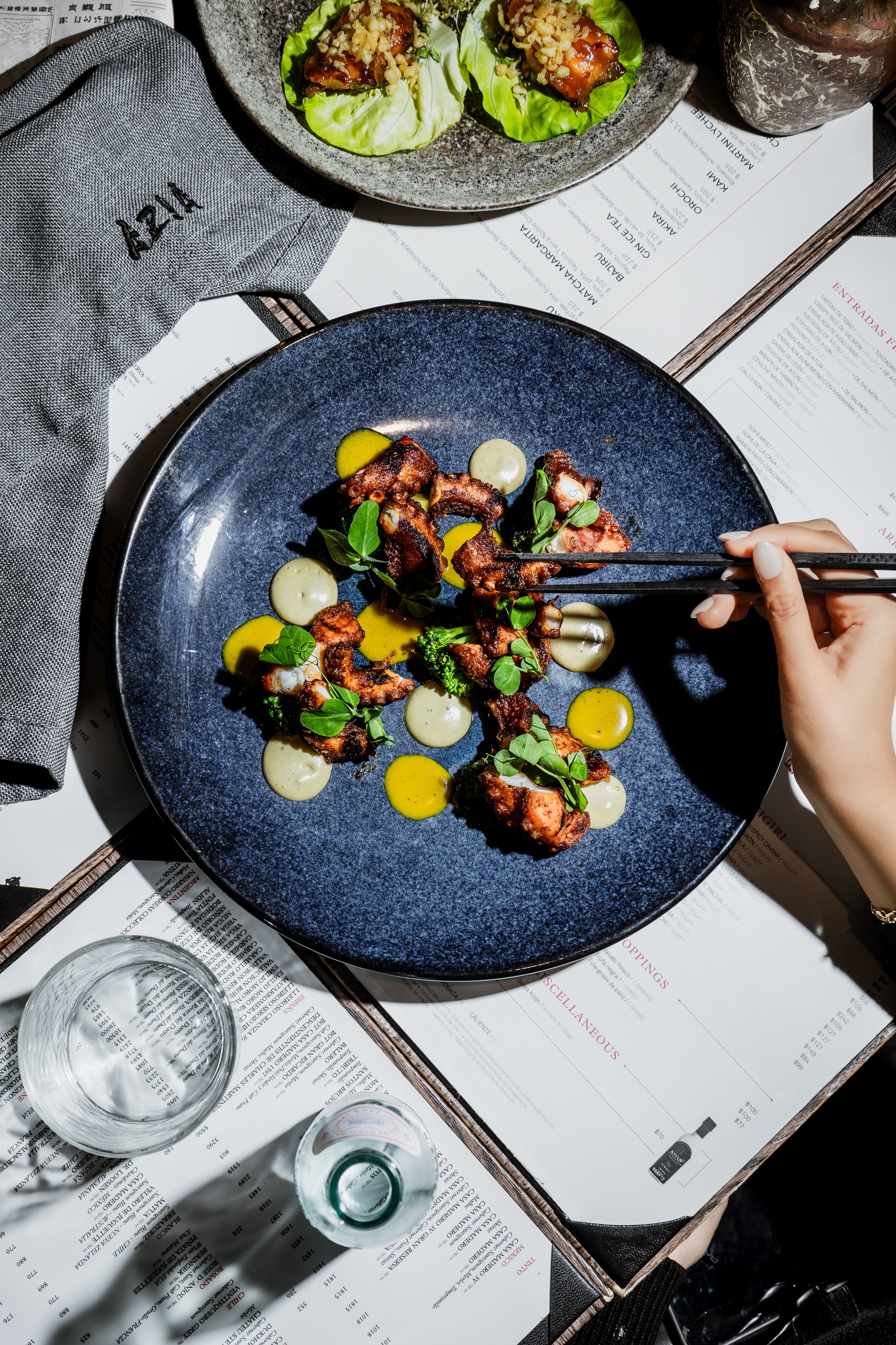 Pulpo servido con hierbas y salsas en un plato oscuro.