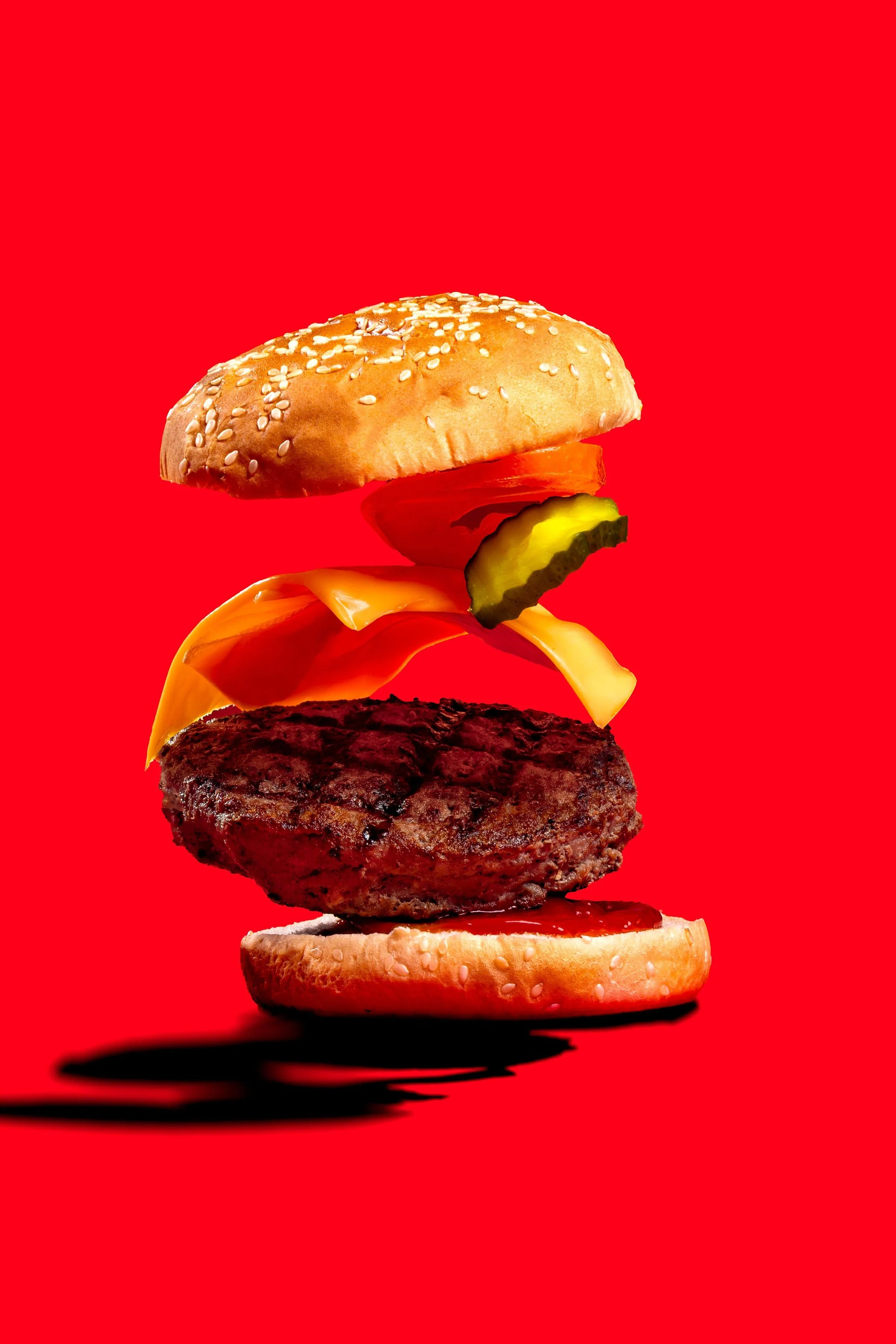 Hamburguesa con ingredientes separados y suspendidos sobre fondo rojo.