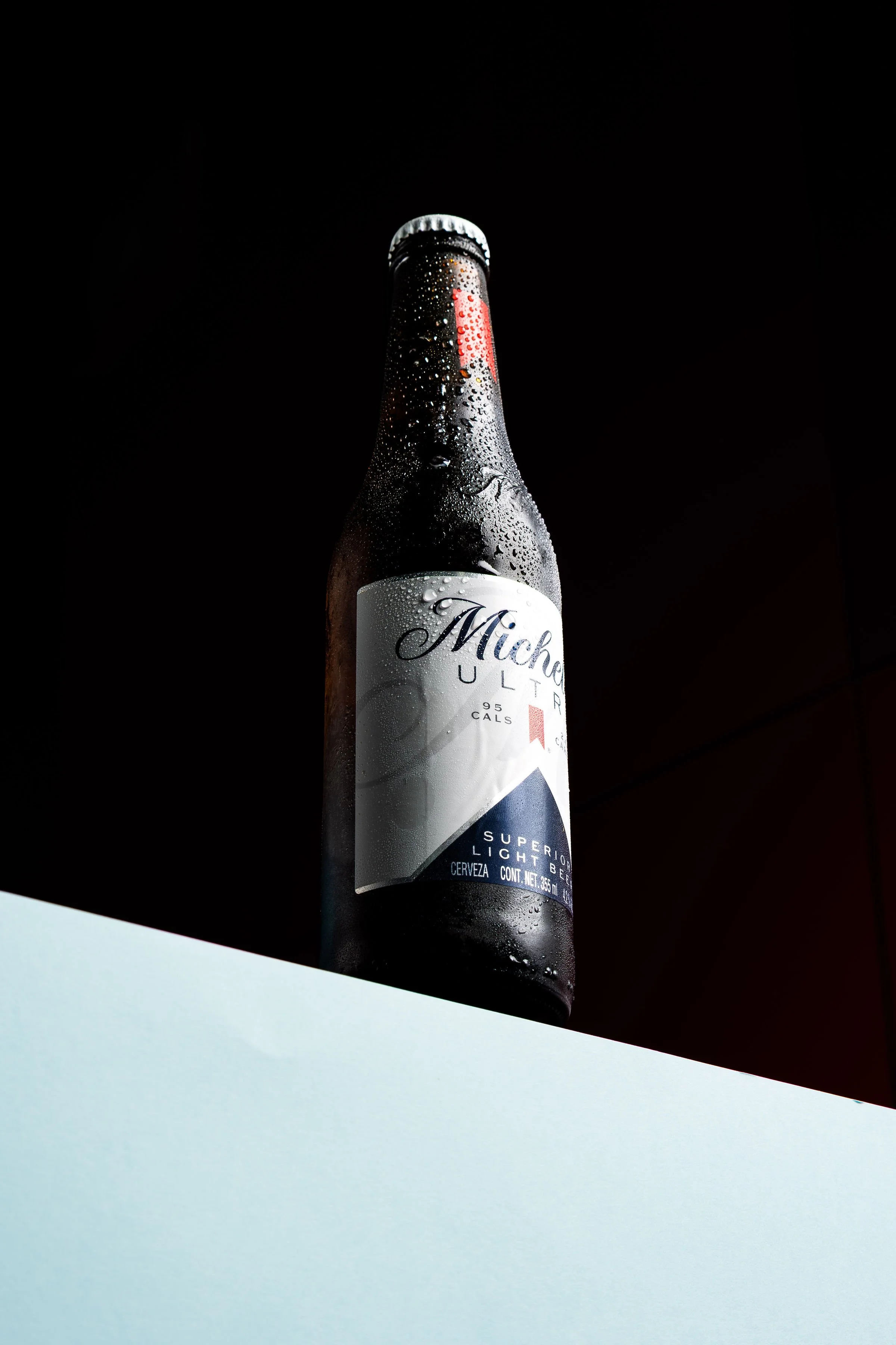 Botella oscura con gotas de condensación e iluminación de contraste.