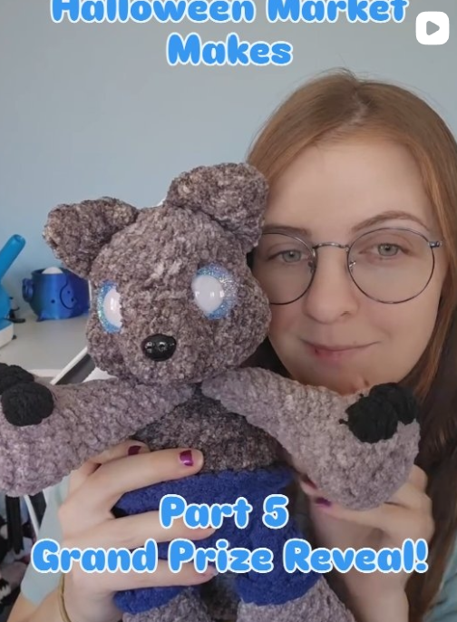 A woman with glasses holding a teddy bear with large round eyes and a black nose. The teddy bear is wearing a blue shirt. There is some text overlay that reads, "Halloween Market Makes Part 5 Grand Prize Reveal!"