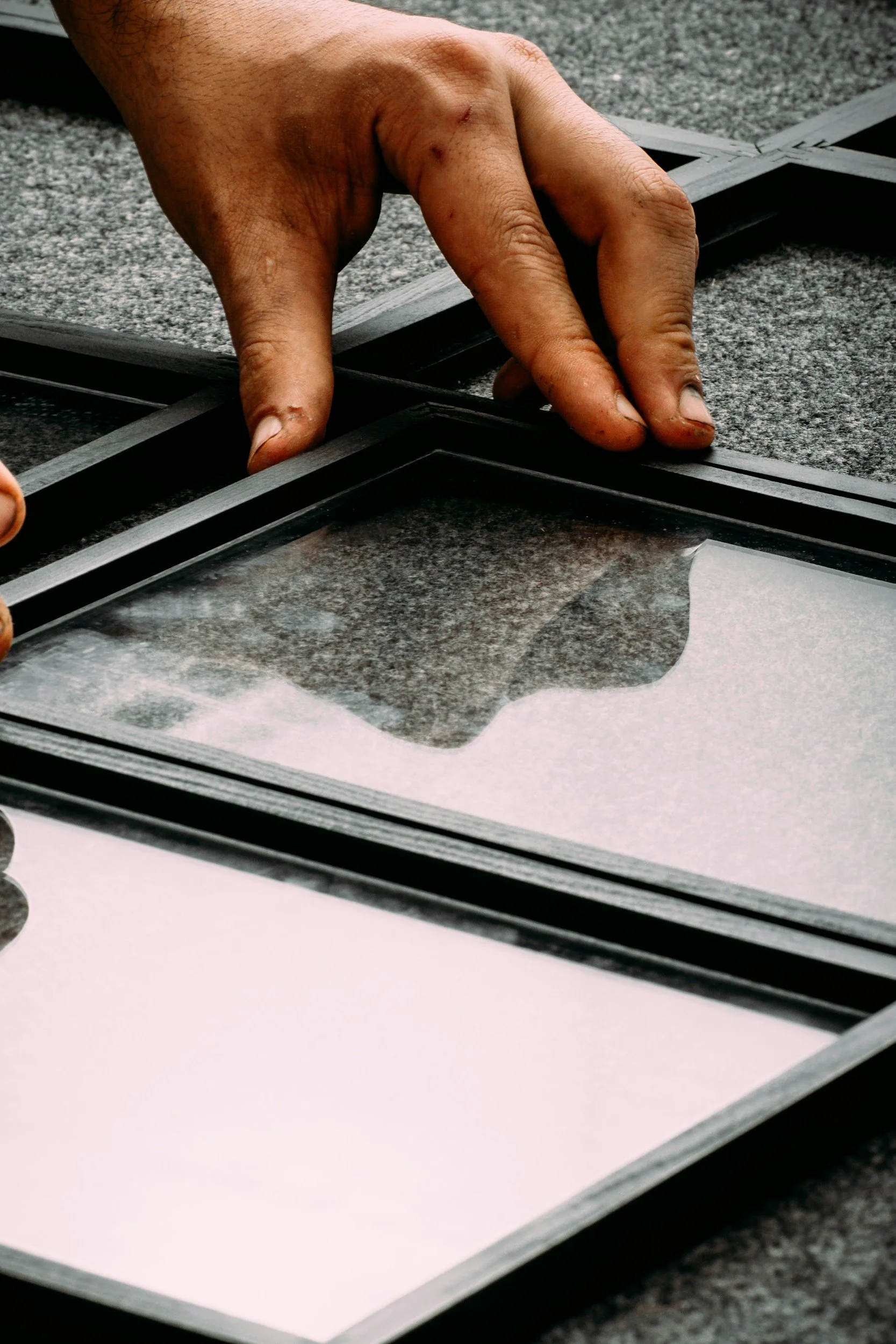 Close-up of a person’s hand assembling black picture frames on a gray textured surface.