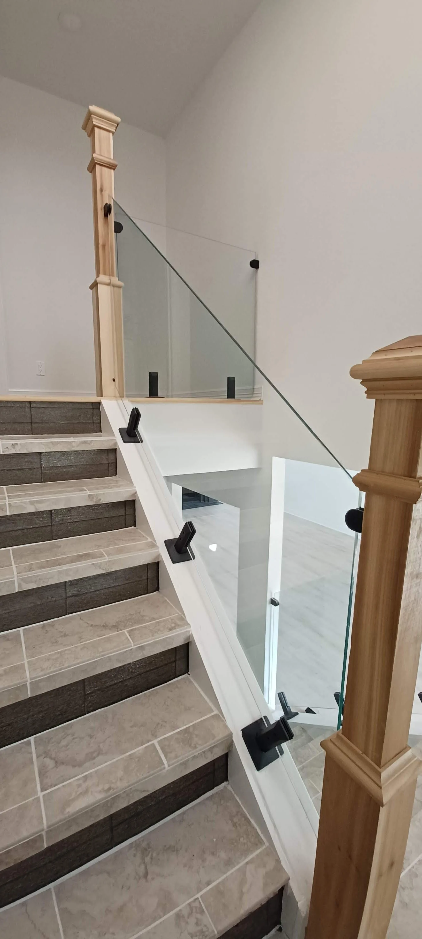 Interior view of a staircase with tiled steps, a glass railing, and wooden newel posts in a home.