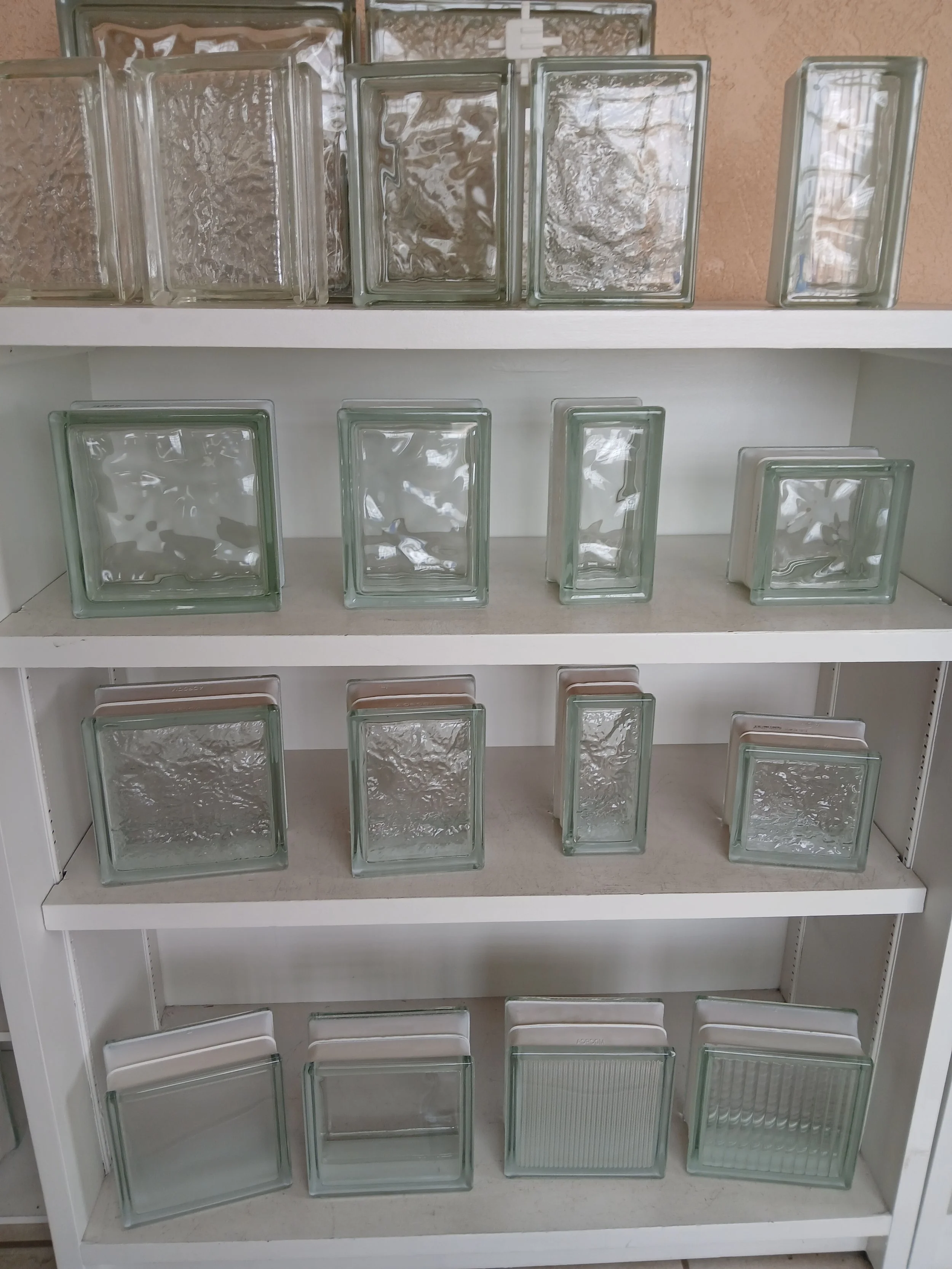 A white shelf with various empty glass blocks of different sizes and textures.