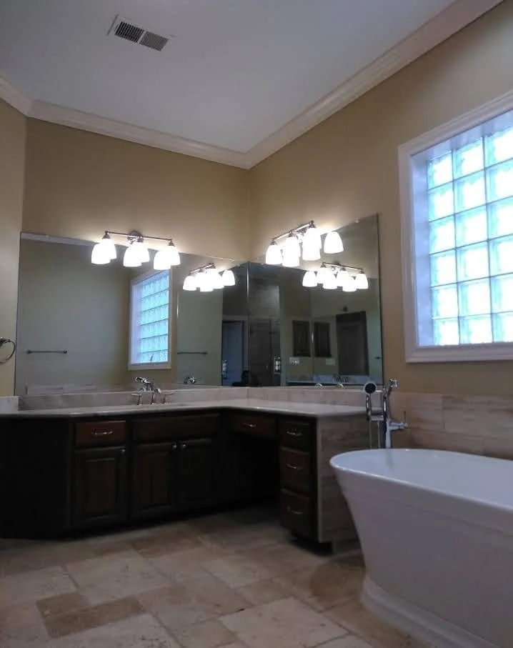 Bathroom with a large mirror, dark wooden cabinets, a bathtub, tiled floor, and a window with glass blocks.