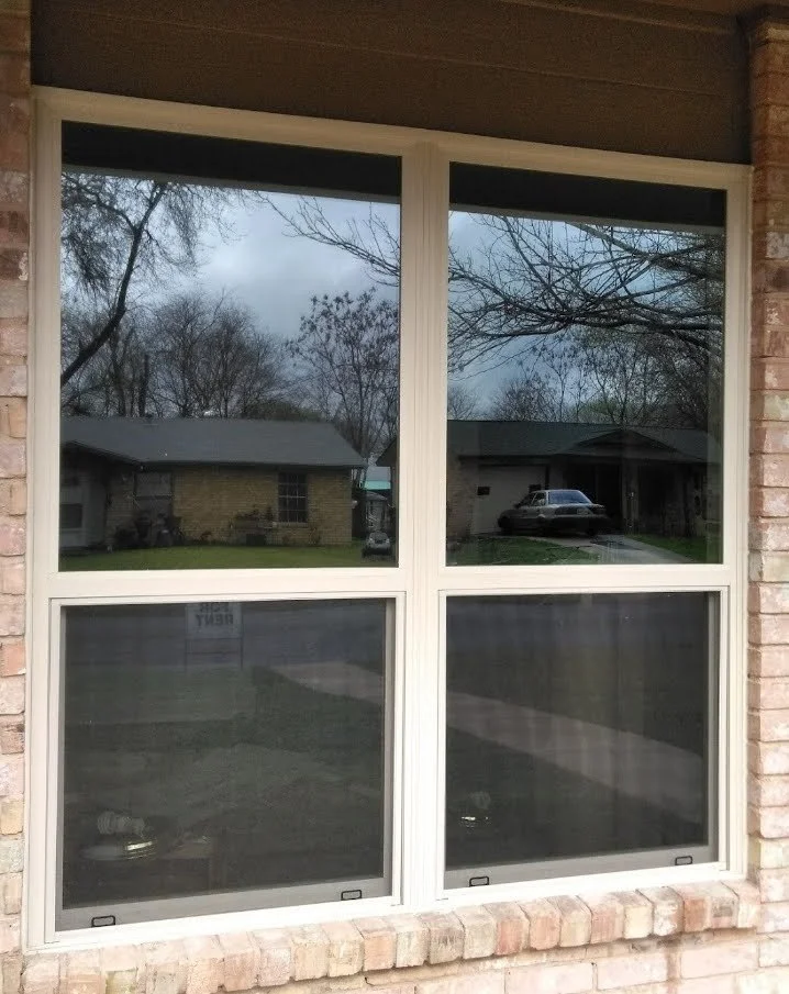 A double-pane window reflection shows neighboring houses, trees, and a parked car on a cloudy day.