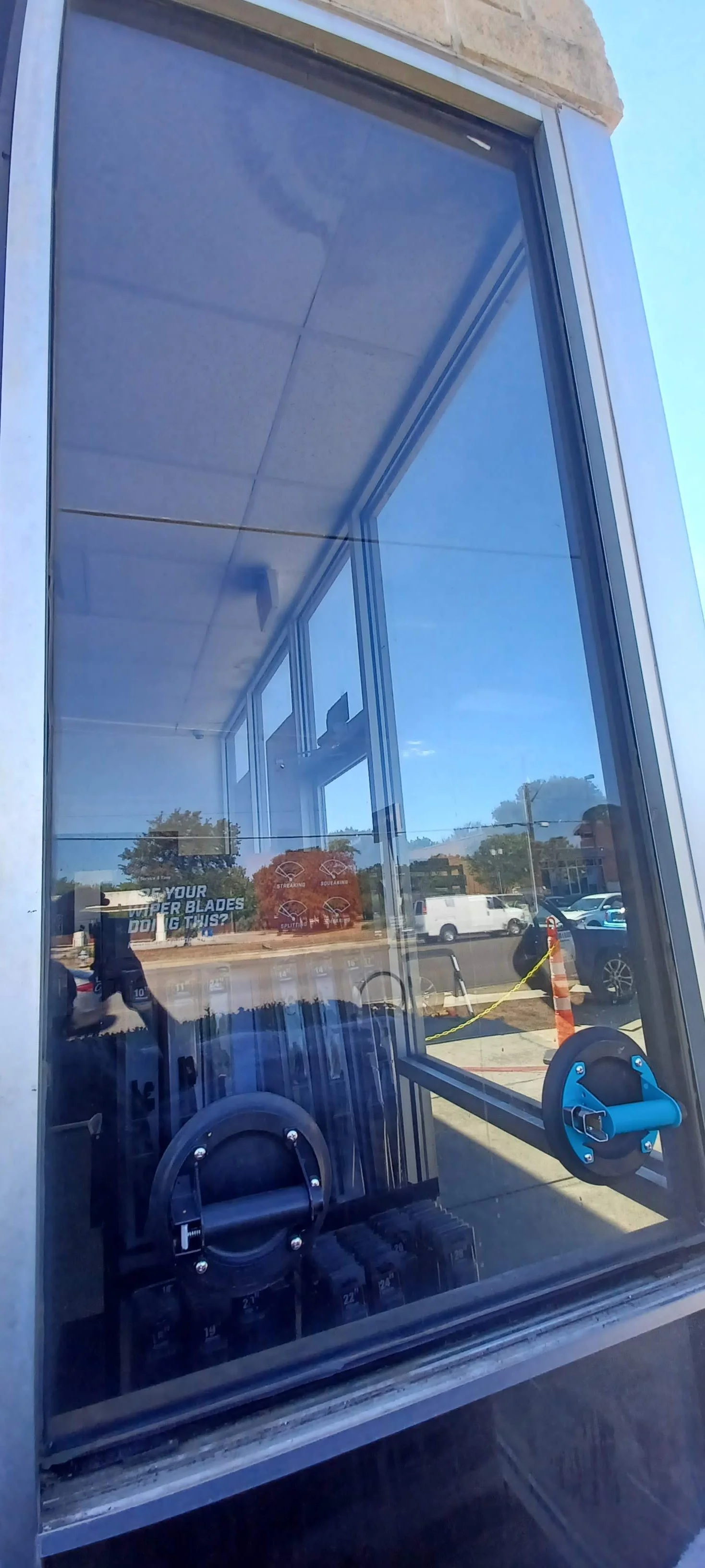 Reflections of cars and trees outside visible through the window of a cleaning machine or display case, with some signage and cleaning tools inside.