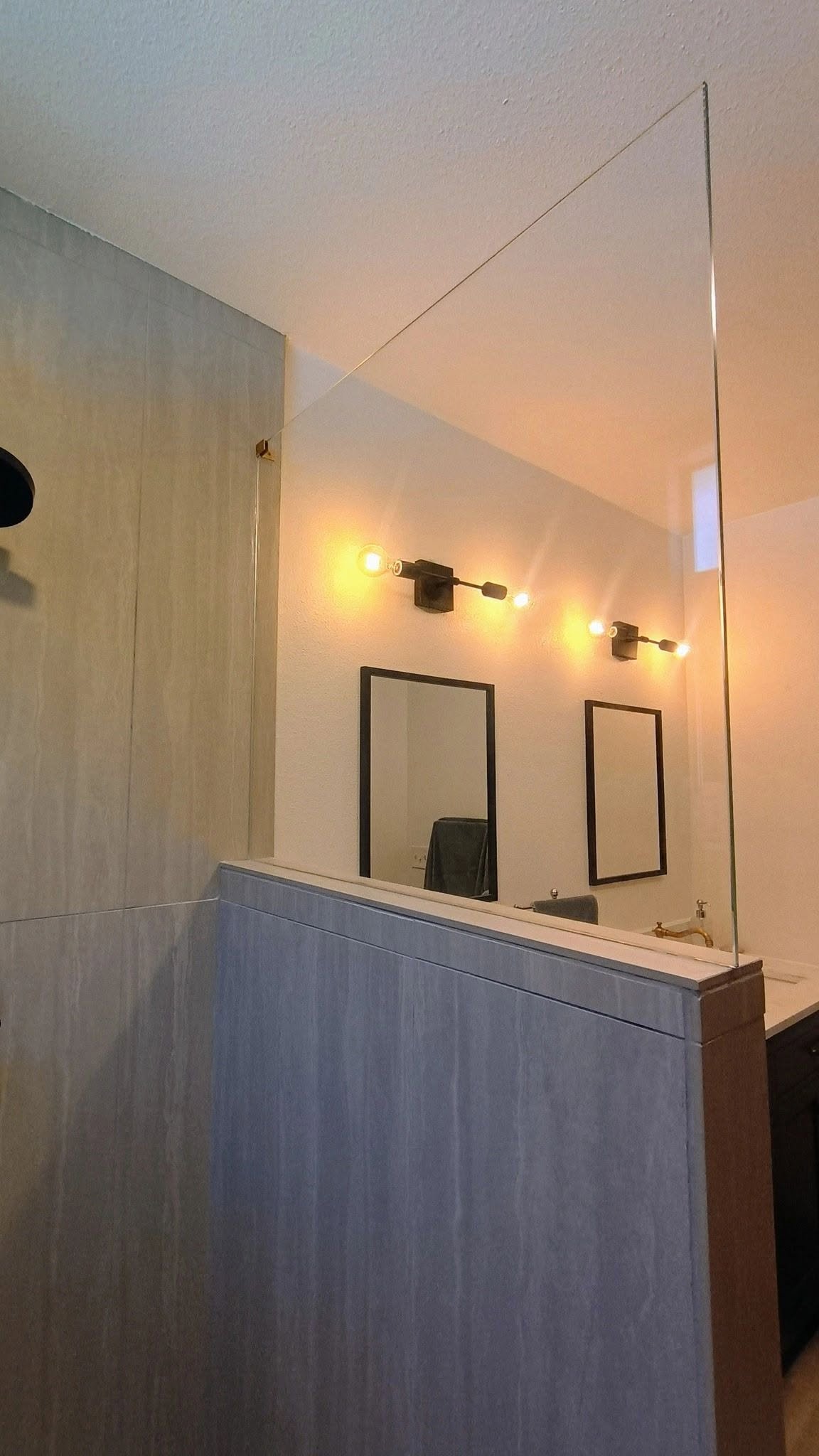 Mirror in a room with warm lighting, black framed pictures on the wall, and a sink with a gold faucet visible in the reflection.