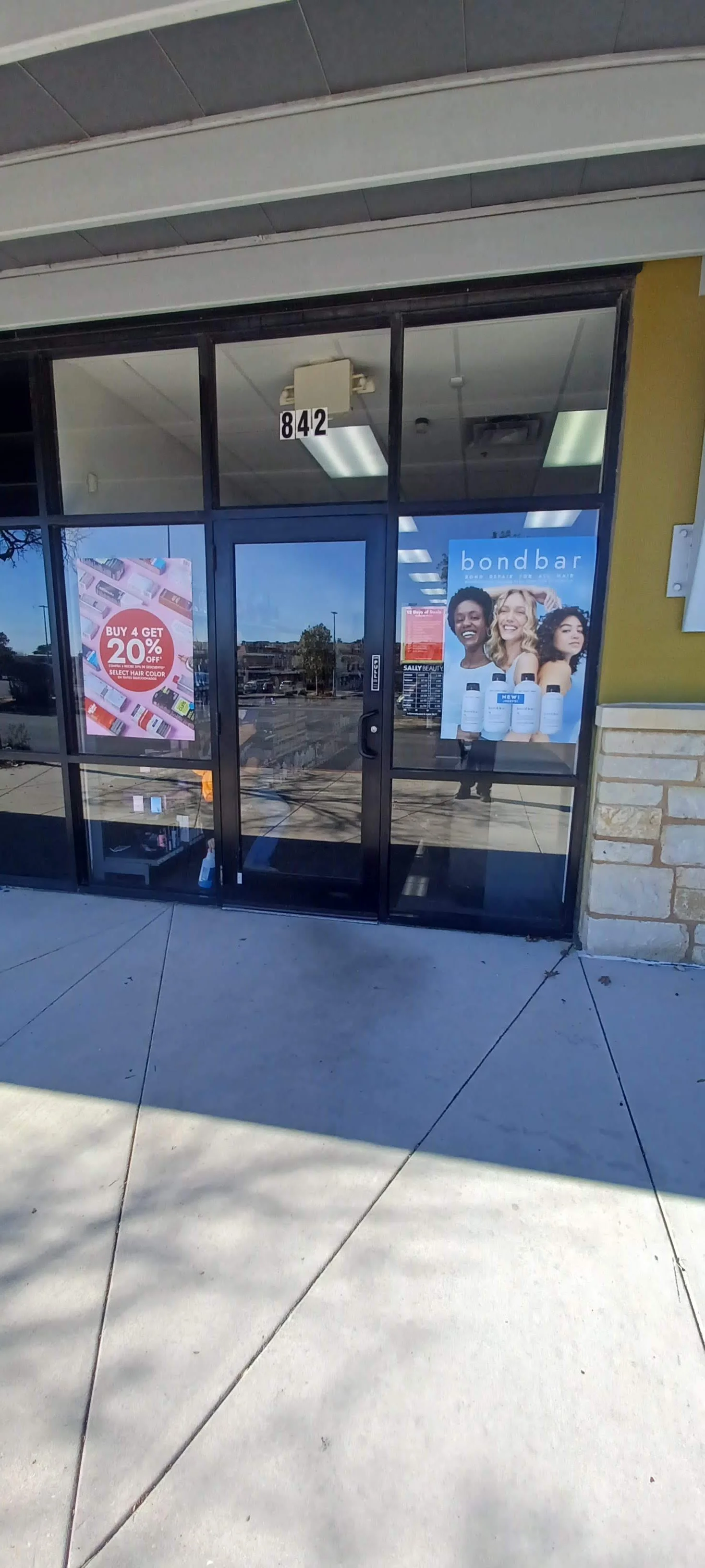 The storefront is made of glass with signs advertising a sale on hair color and beauty products. The store number 842 is in the top window, and there are posters of smiling women and bottles of hair care products inside.