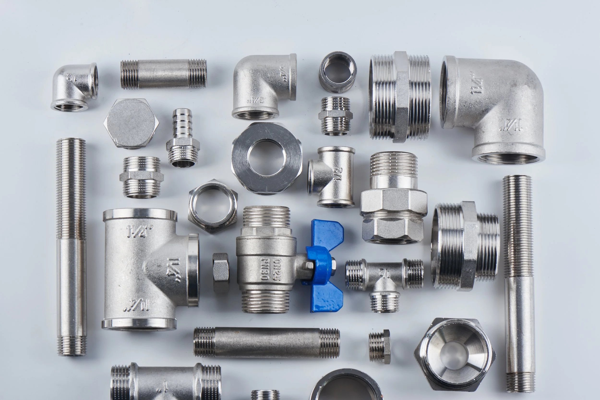 A collection of metal plumbing fittings, including elbows, connectors, and threads, laid out on a light background.