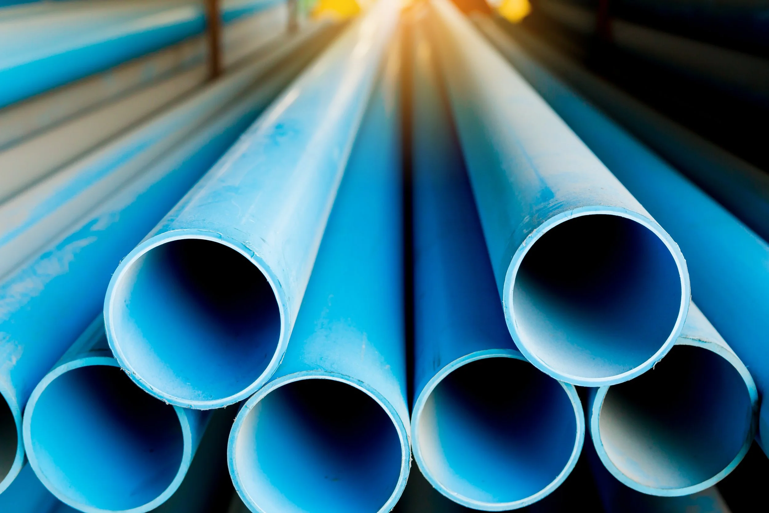 Close-up of blue plastic pipes stacked together with sunlight shining in the background.
