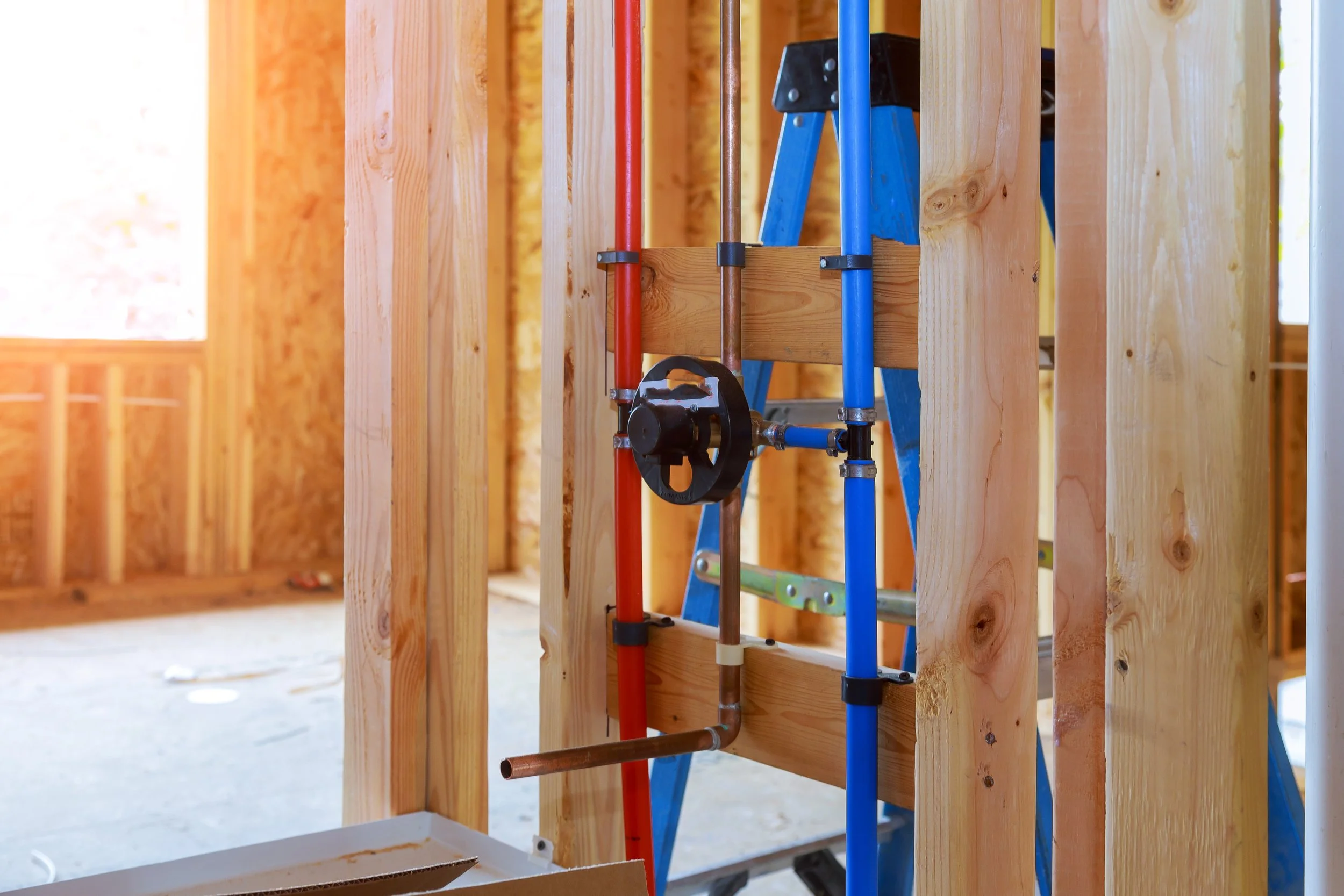 View of plumbing pipes installed within wooden framing of a building under construction.