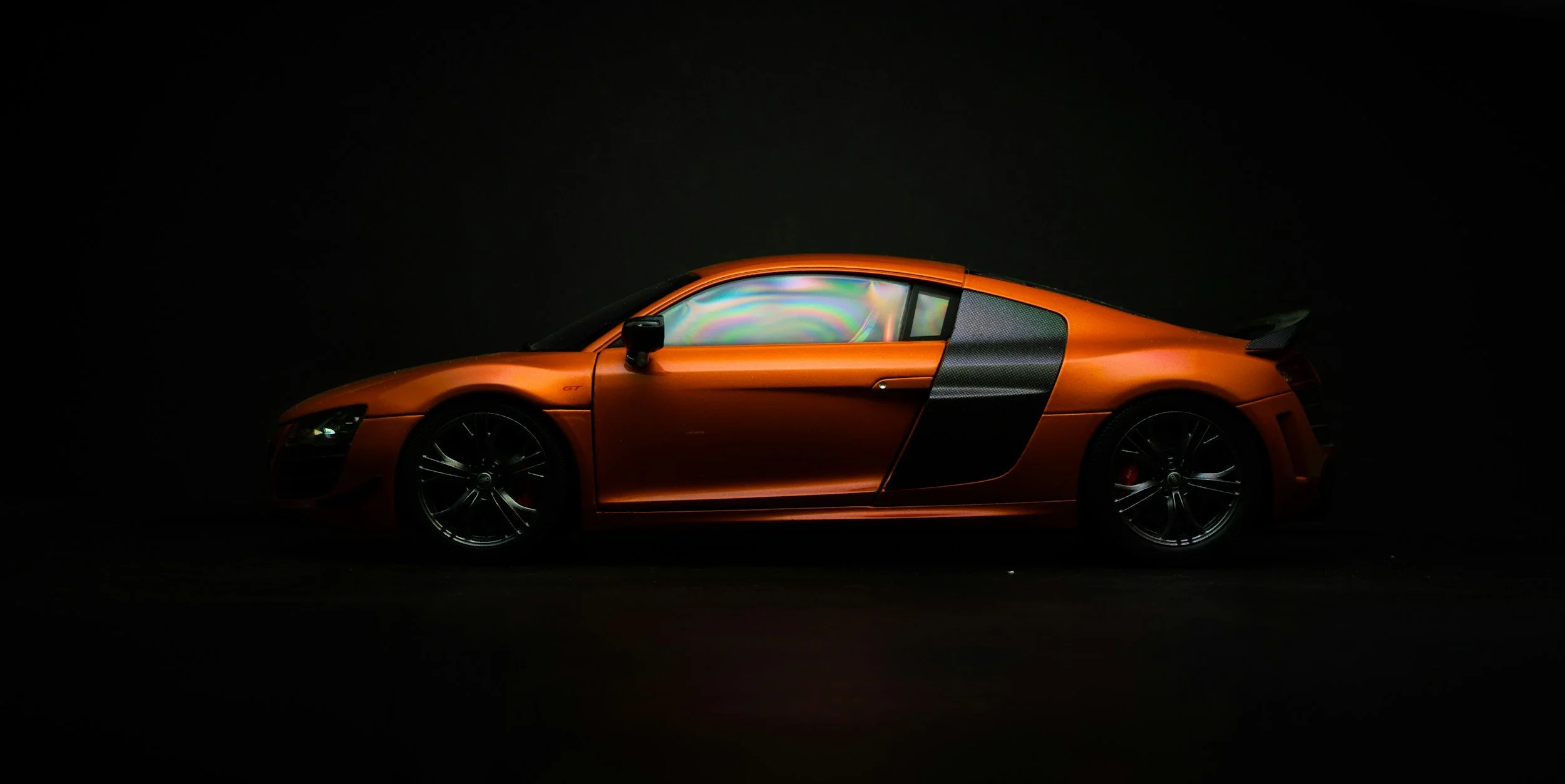 A sleek orange sports car with black accents is shown in a dark environment, highlighting its design and detail.