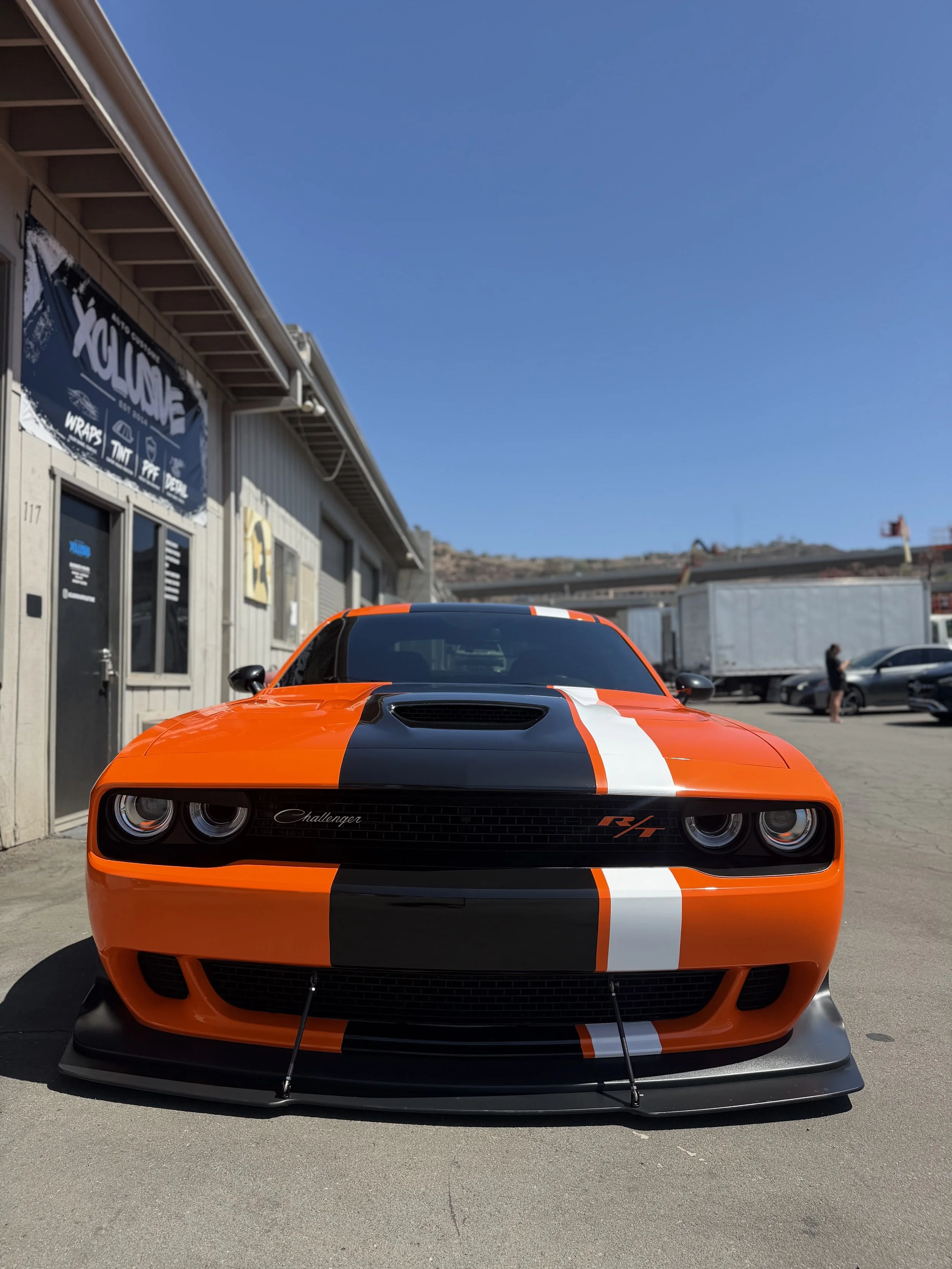 Orange Dodge Challenger with black and white racing stripes wrapped at Xclusive Auto Customz in Santee, CA