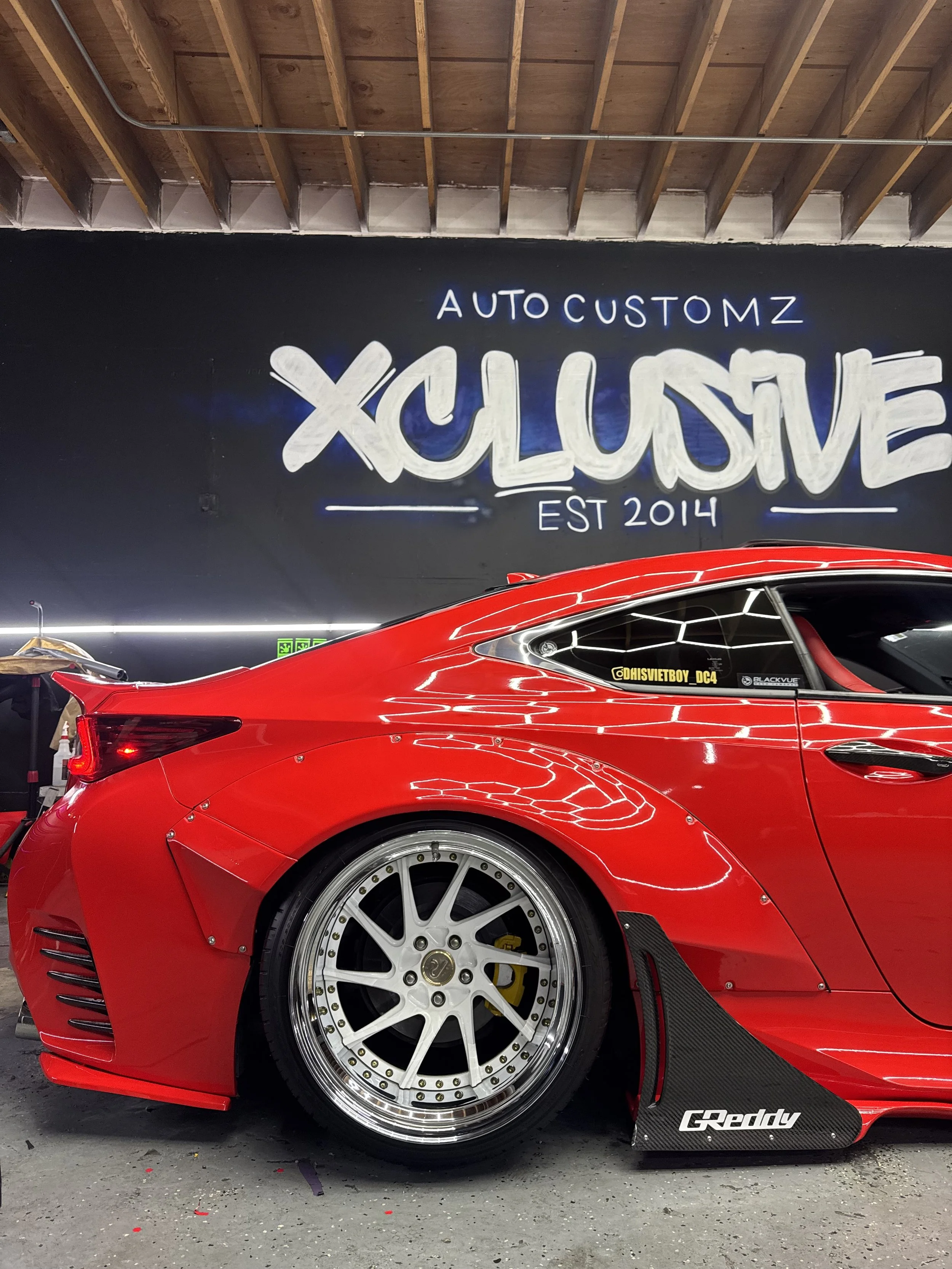Red Lexus RC coupe with custom wrap in front of Xclusive Auto Customz shop sign in Santee, CA