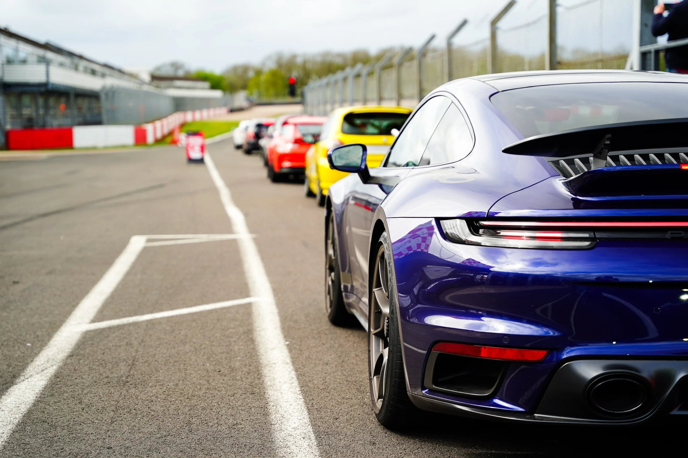 Line of sports cars parked at a racetrack, with the closest being a purple and black car.