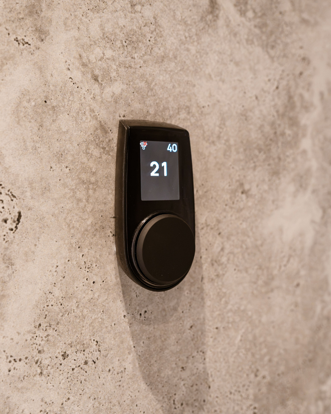 A digital thermostat on a textured beige wall showing a temperature of 21 degrees.