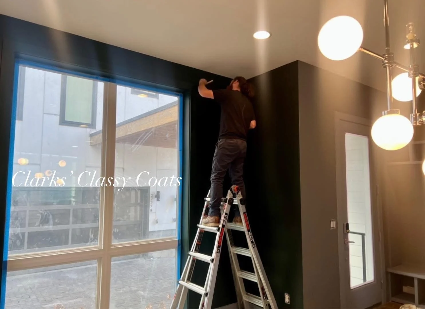 Evan painting a dark accent wall beside a large window