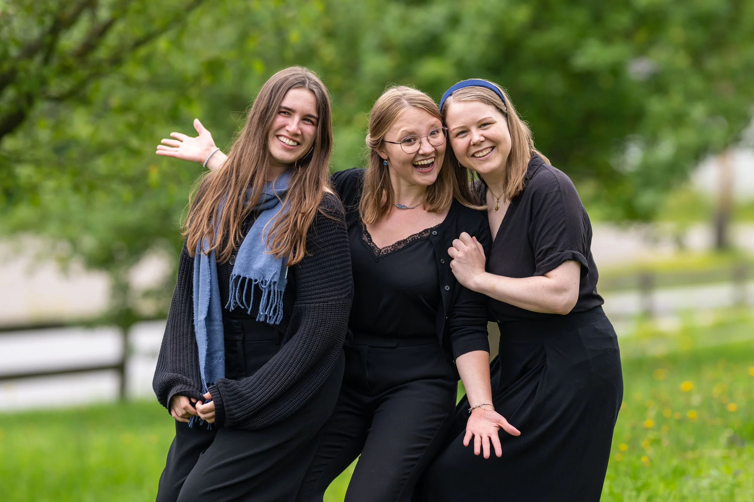 Drei lachende Frauen beim Spaziergang im Park, umarmend und fröhlich, mit grünen Bäumen im Hintergrund.