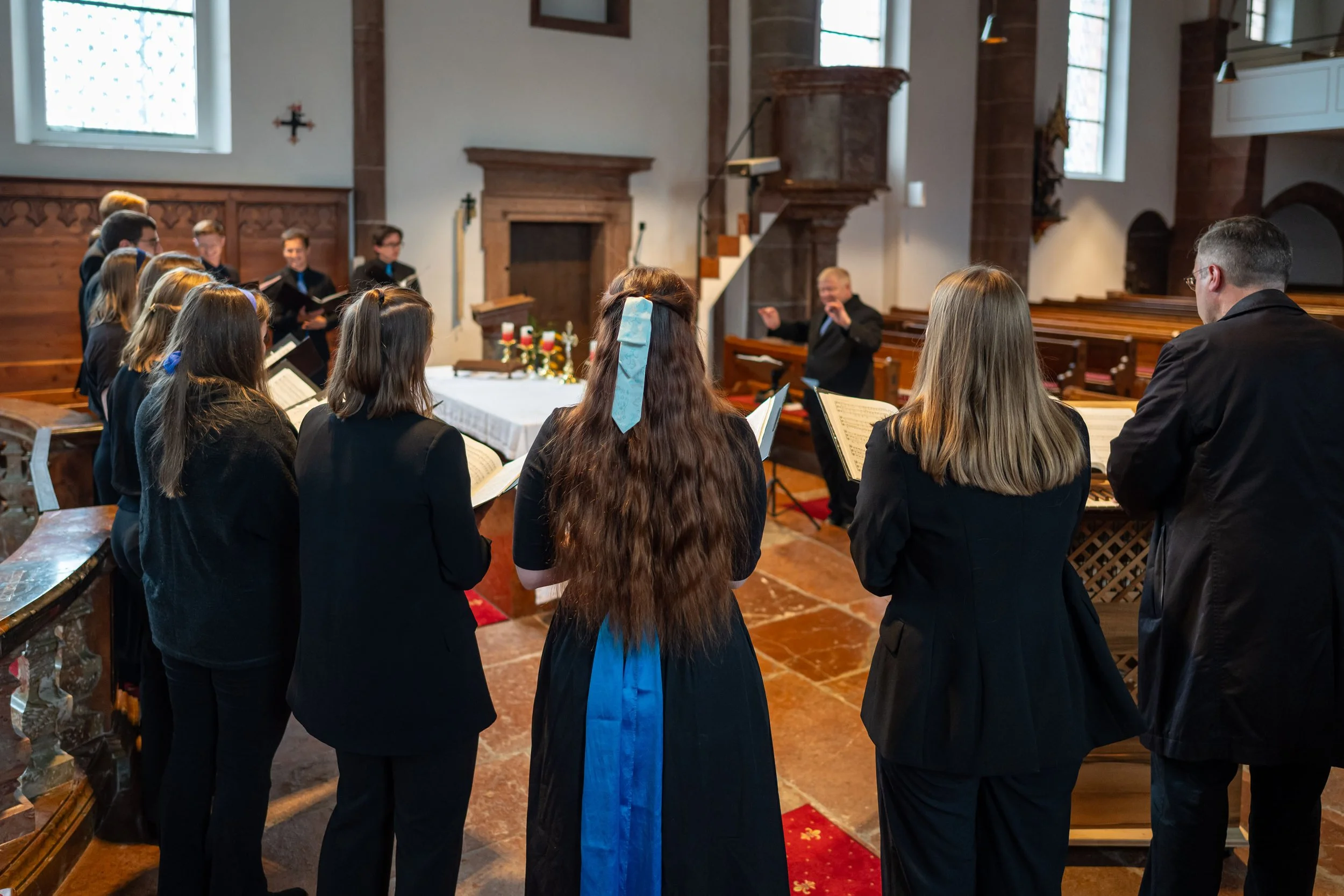 Chor, der in einer Kirche singt, während der Dirigent dirigiert, mit einer Dekoration auf dem Altar.