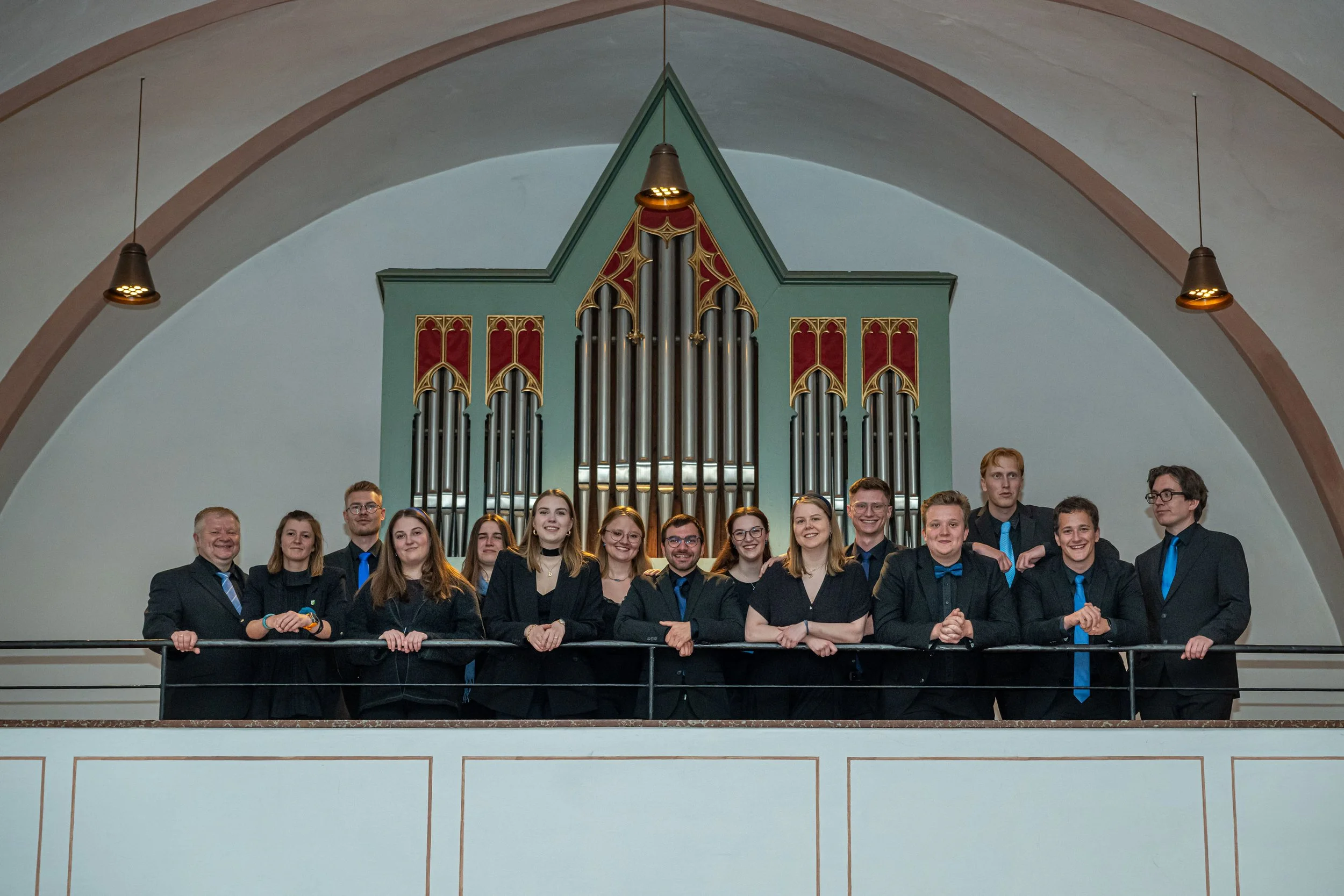 Gruppe von jungen Erwachsenen und einem älteren Mann vor einer Orgel in einer Kirche, alle tragen formelle Kleidung, einige tragen blaue Krawatten, smiling, Gruppenfoto