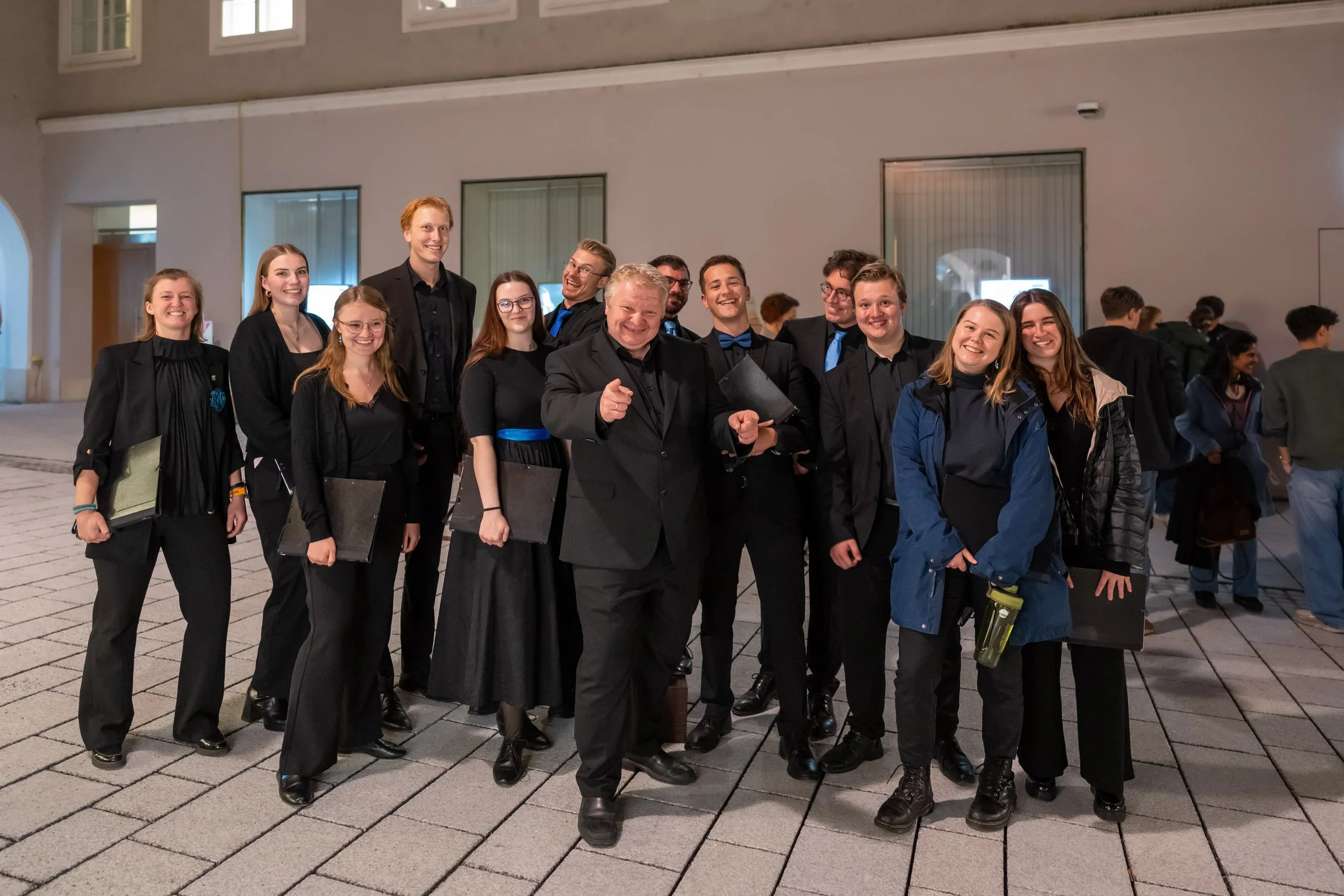 Eine Gruppe von Menschen, vor allem junge Erwachsene, die in formeller Kleidung stehen und lachen. Es scheint, dass sie in einem öffentlichen Gebäude oder bei einer Veranstaltung sind.