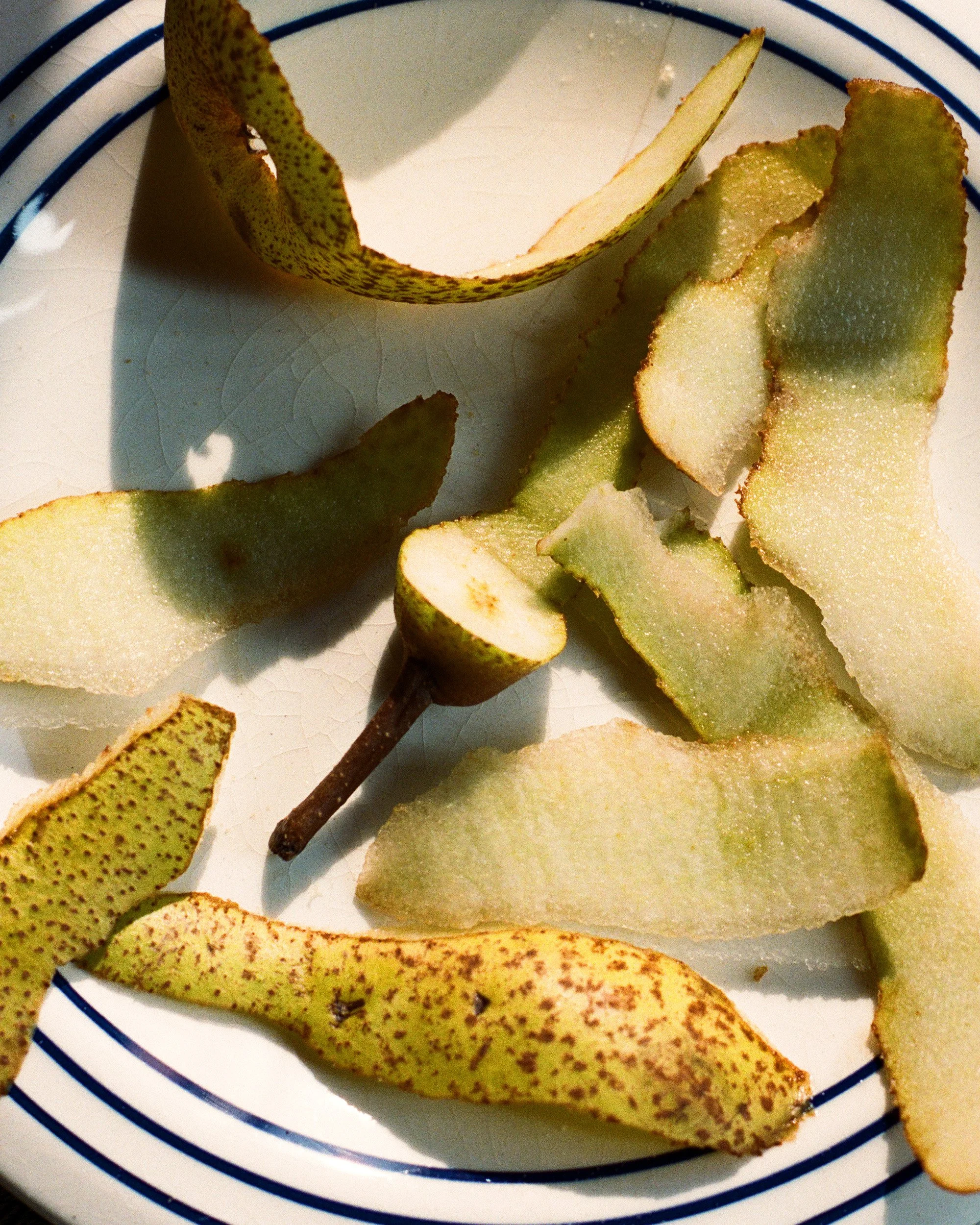 Slices of a green pear with brown speckled skin on a white plate with blue lines.