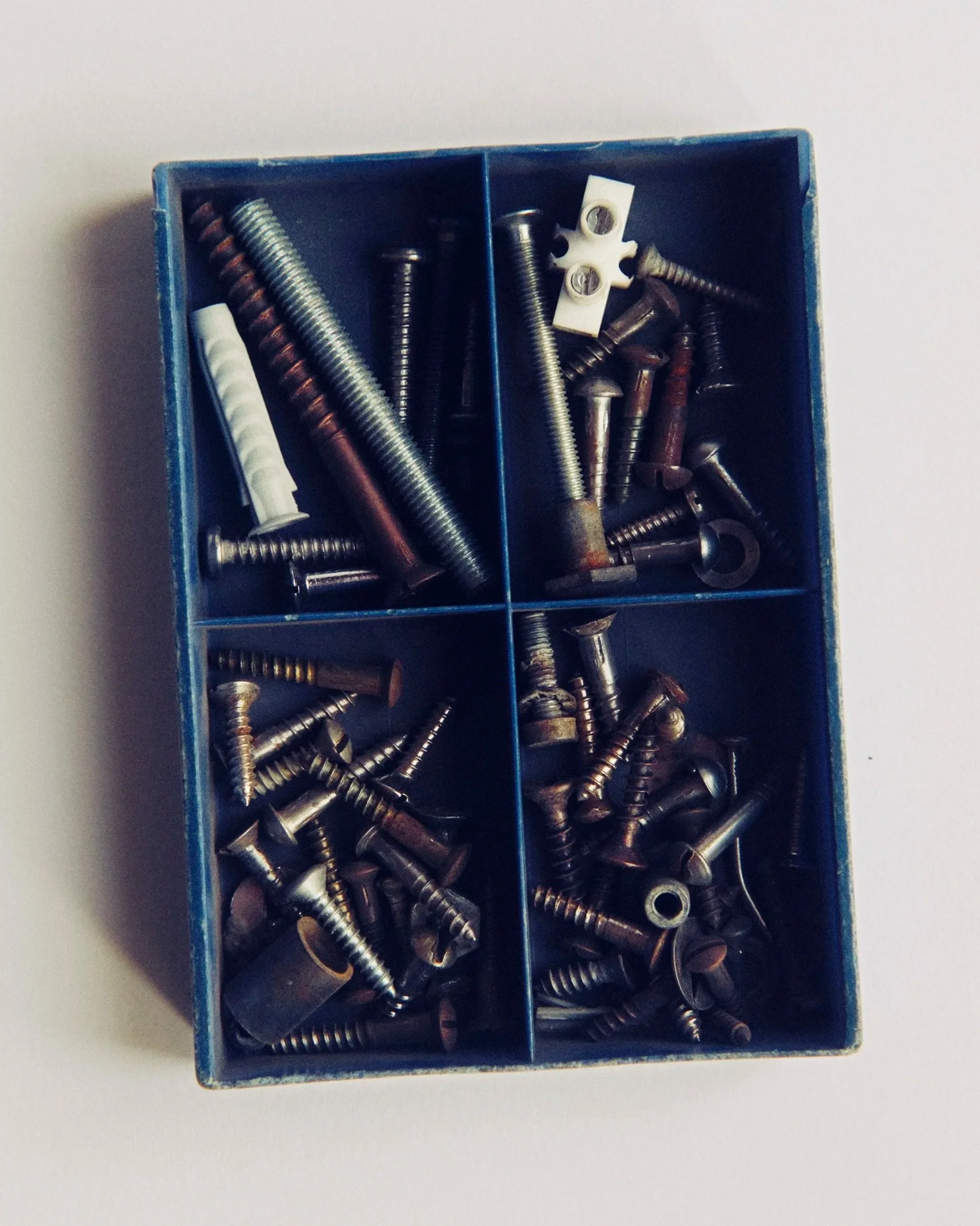 A metal storage box with multiple compartments filled with various screws and fasteners.