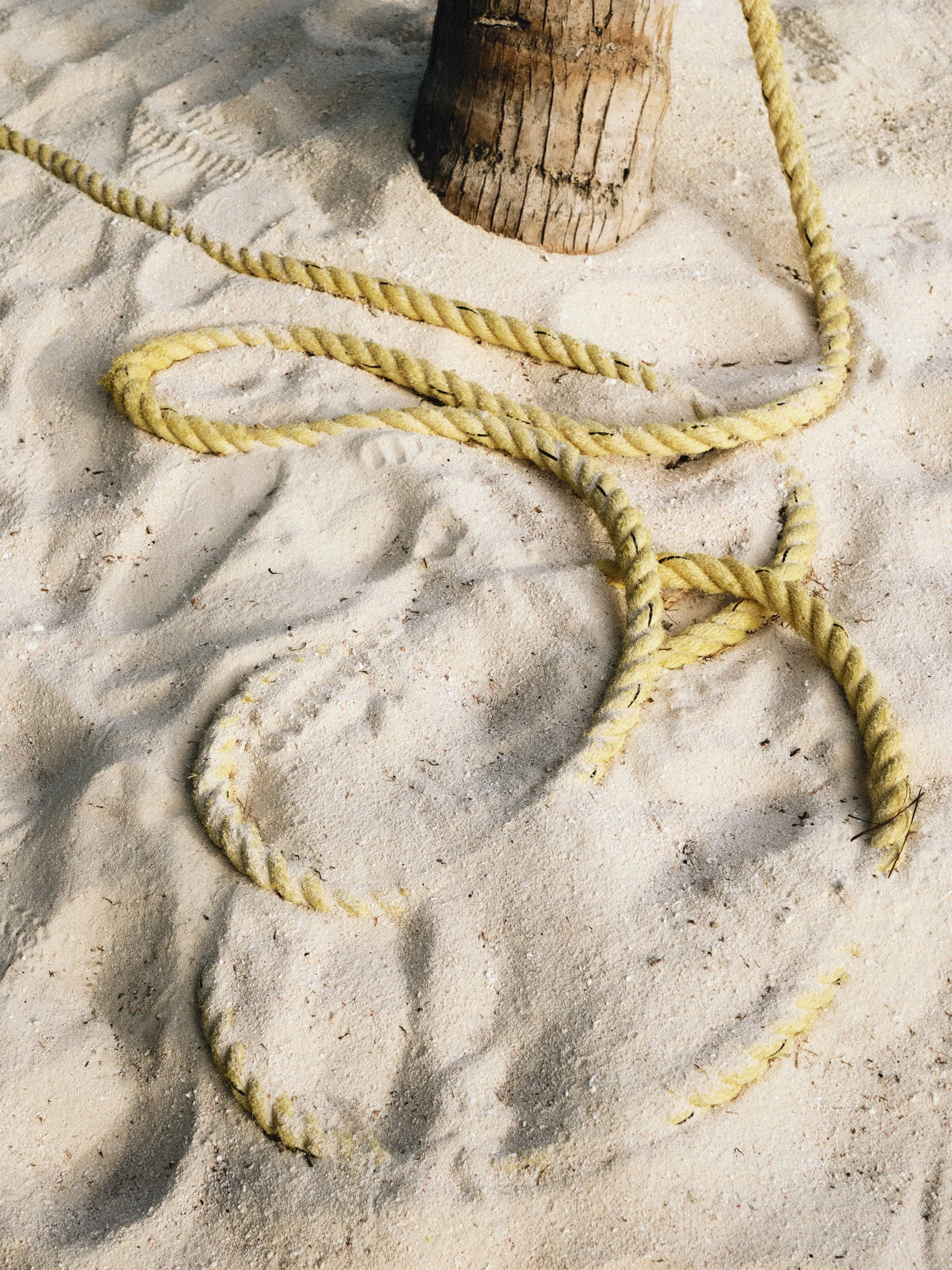 A close-up of a sandy beach with a piece of yellow rope and the base of a wooden post.