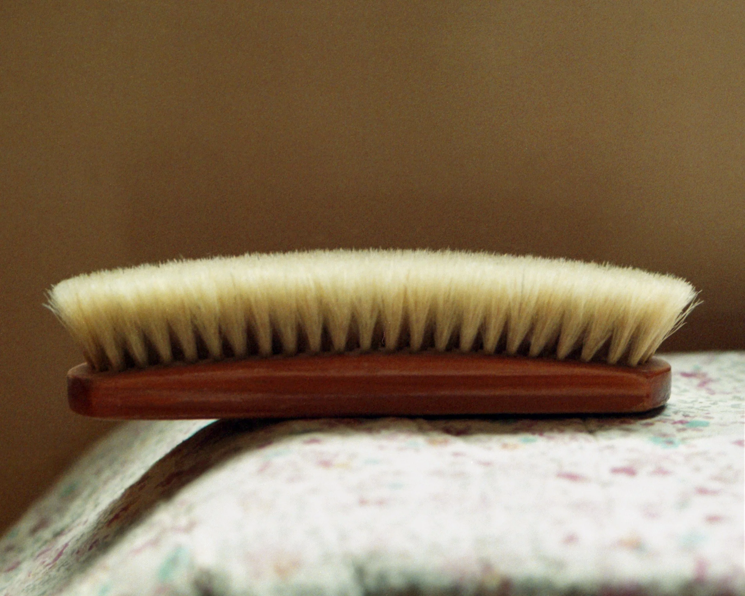 Close-up of a toothbrush with white bristles on a wooden base, resting on an ironing board with a floral fabric cover.