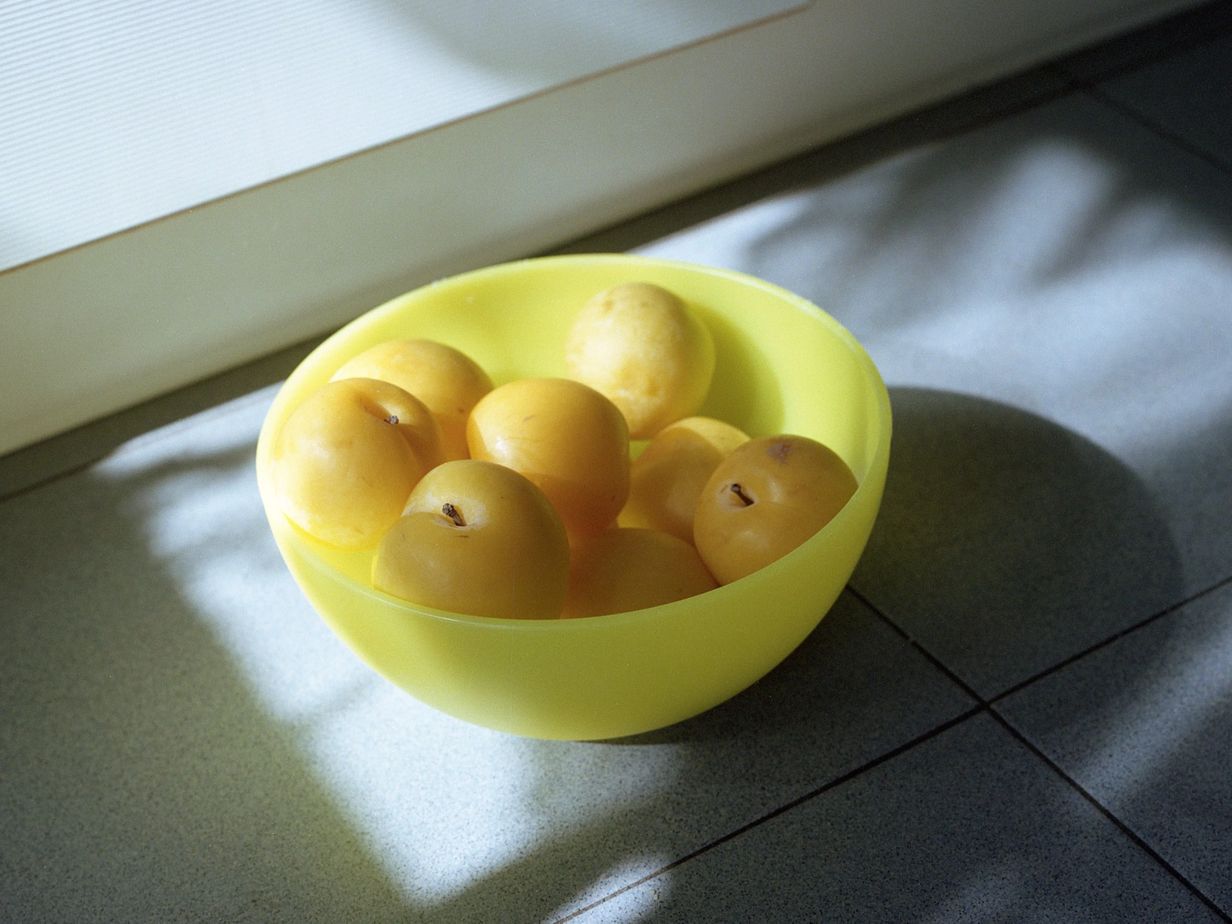 Yellow bowl filled with yellow apples sits on a kitchen counter near a window.