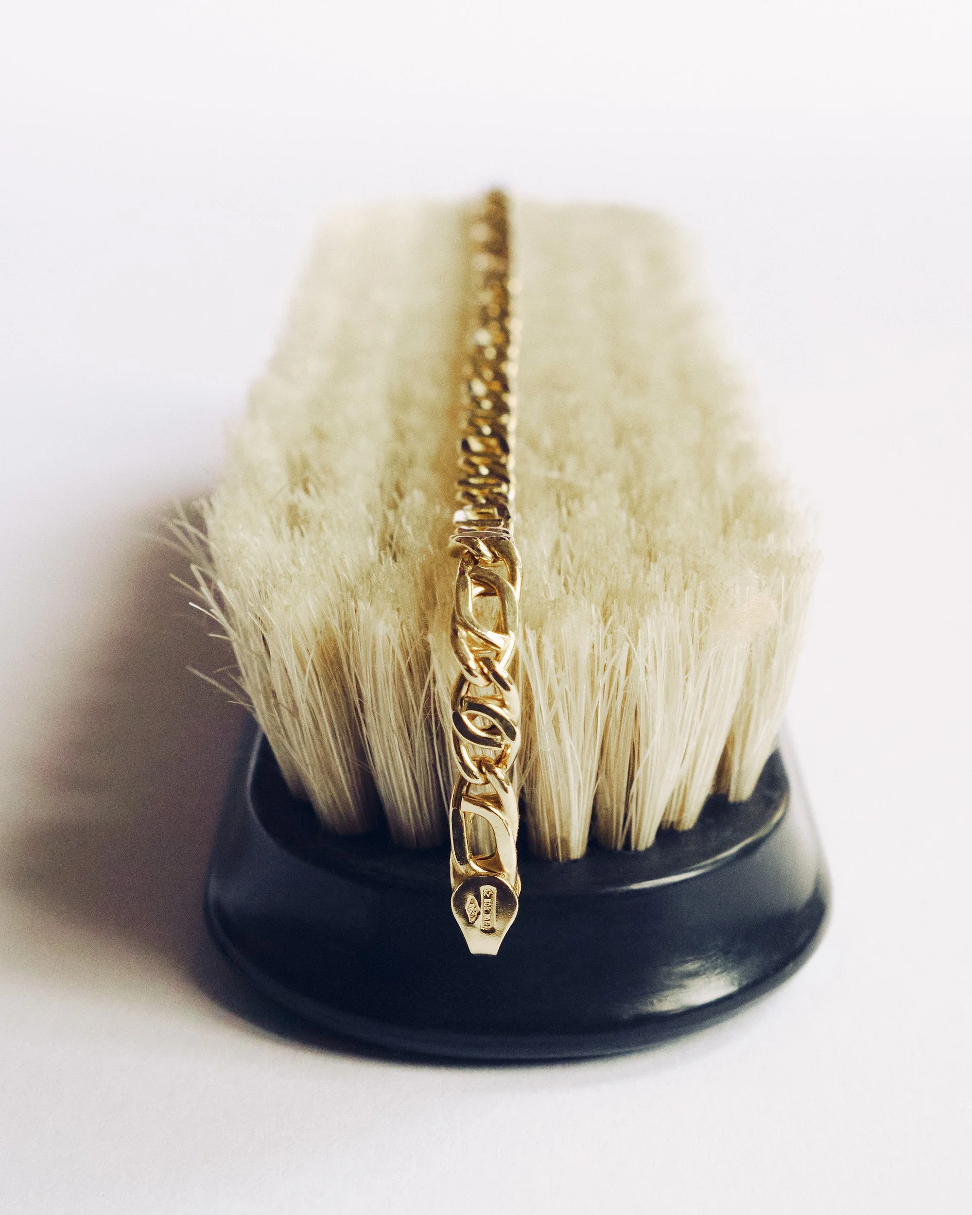 Close-up of a gold chain necklace resting on a barber brush with white bristles and a black handle.