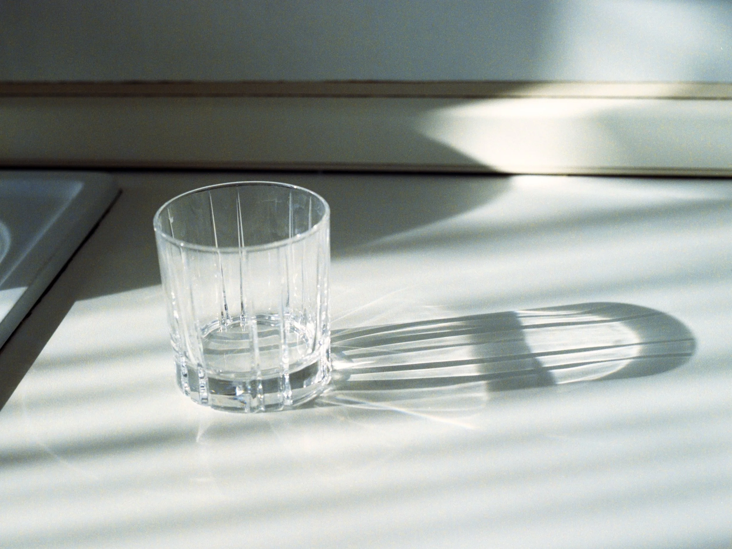 A clear, empty plastic cup on a white surface with a shadow cast by sunlight.