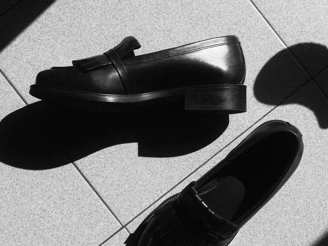 Black leather loafers on a tiled floor with shadows.