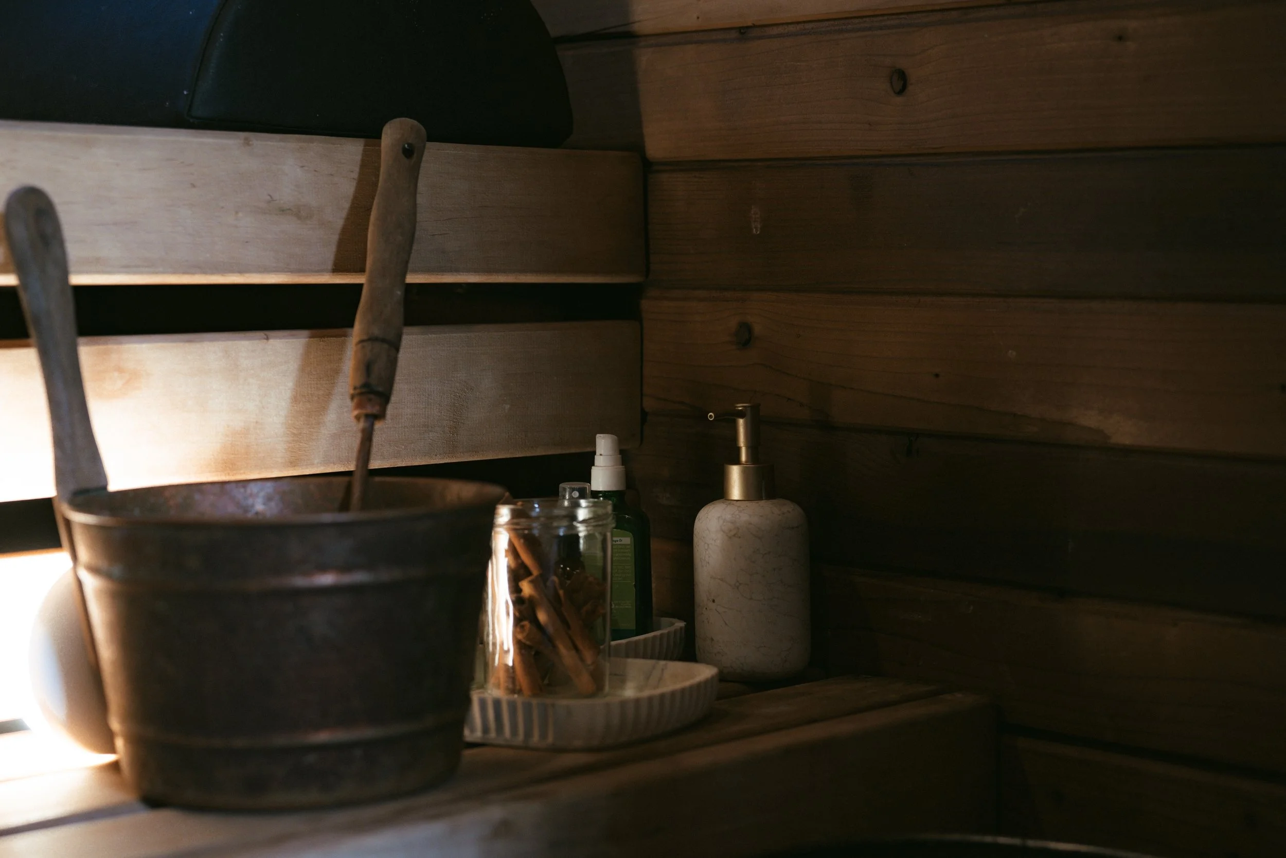 Blick auf eine Holzregalwand mit Küchenutensilien, darunter eine Messing-Seifenspender, eine Kerze und ein Glas mit Streichhölzern, Beleuchtung von links.