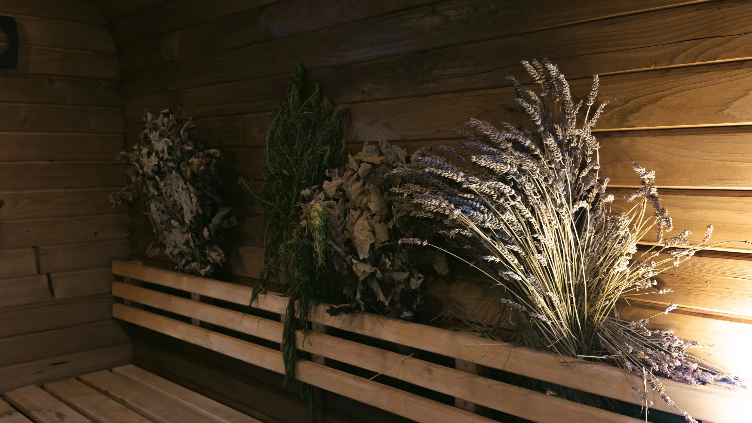 Bündel getrockneter lavenderfarbener Blumen vor einer Holzvertäfelung.