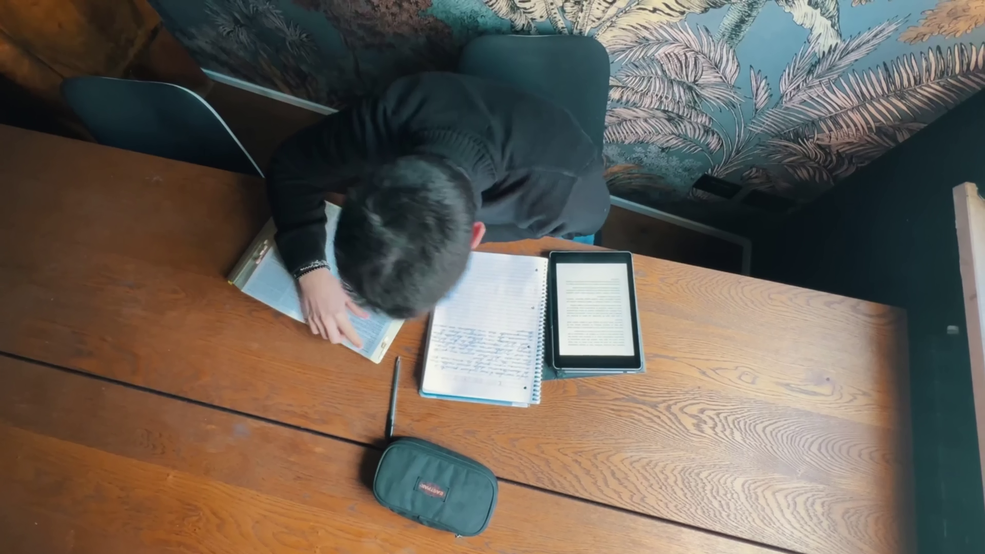 Seba seduto ad un tavolo di legno, studiando sui libri di latino tra le mura della sua casa. Immagine di anteprima tratta dal cortometraggio "Caesena me cecidit".