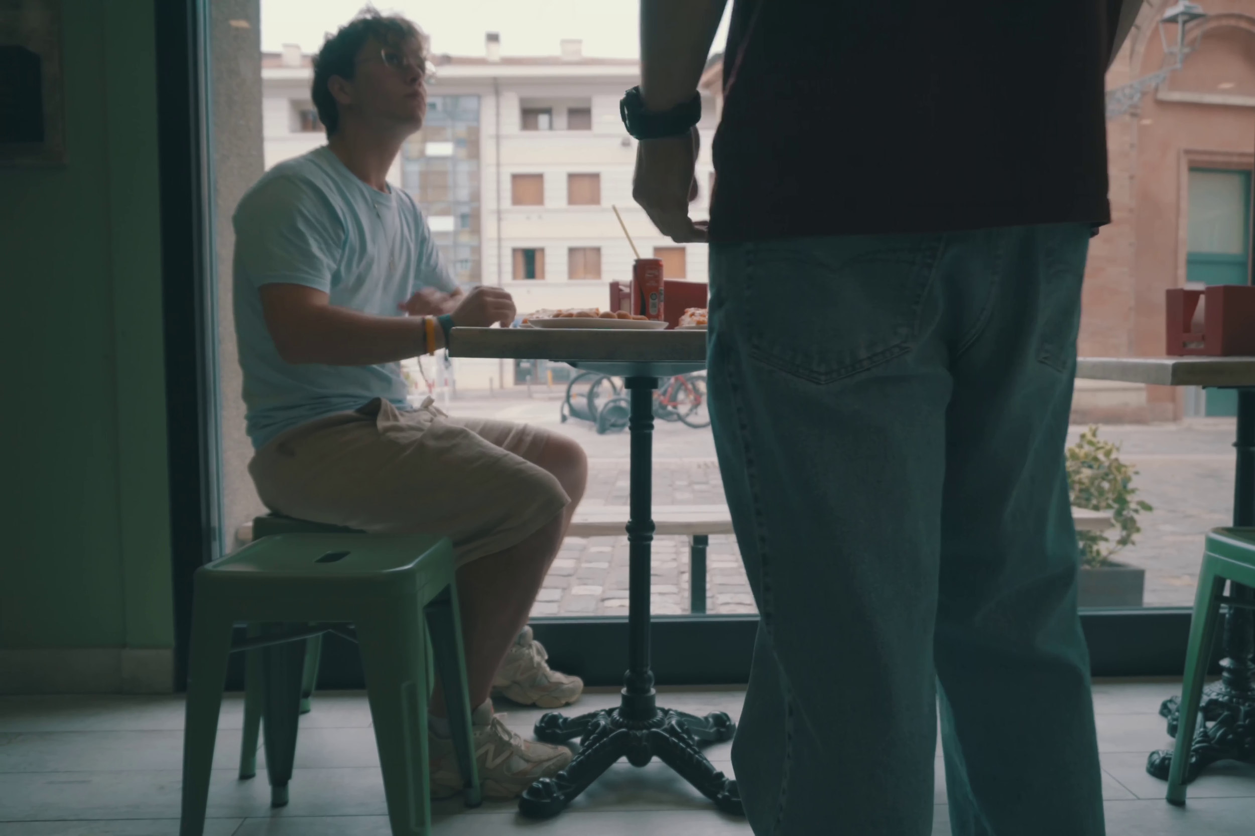 Max (interpretato da Giacomo Petit) è seduto al tavolo di una pizzeria con le pareti color azzurro chiarissimo, davanti a lui ci sono già delle pizze, e Stills è appena arrivato, ancora deve sedersi.