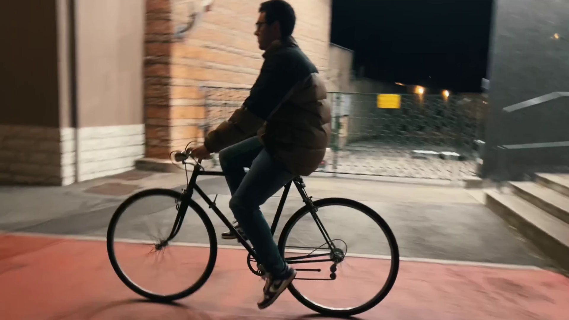 Seba (interpretato da Kristian Dedja) che pedala su una bicicletta di sera o di notte, con un edificio in background e la strada illuminata. Immagine di anteprima tratta dal cortometraggio "Caesena me cecidit".