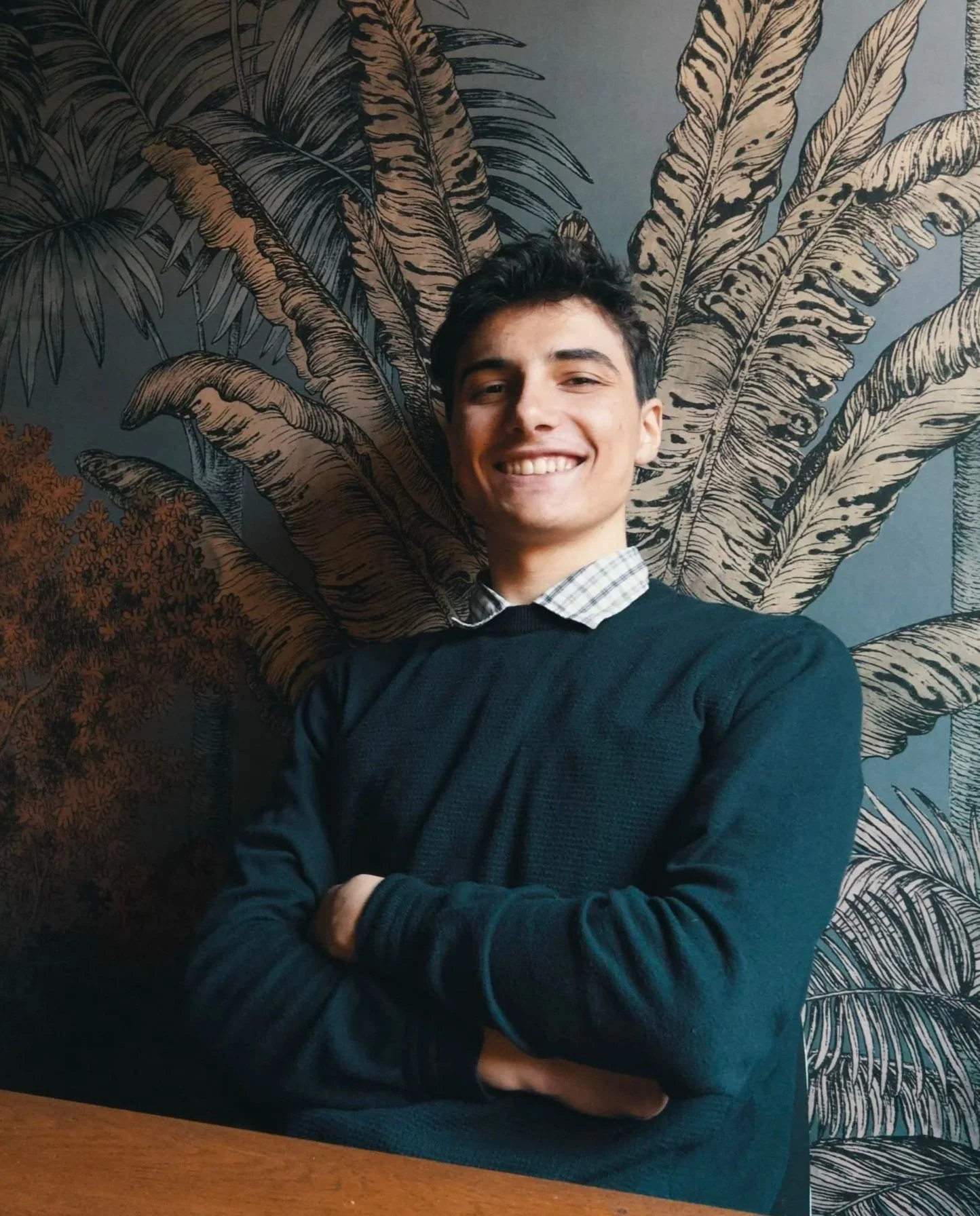 Immagine di presentazione dello storyteller e filmmaker Gael Angelini: ritratto di mezzobusto con le braccia incrociate, i capelli un po' disordinati e sorridente seduto ad un tavolo dal set di "Caesena me cecidit".